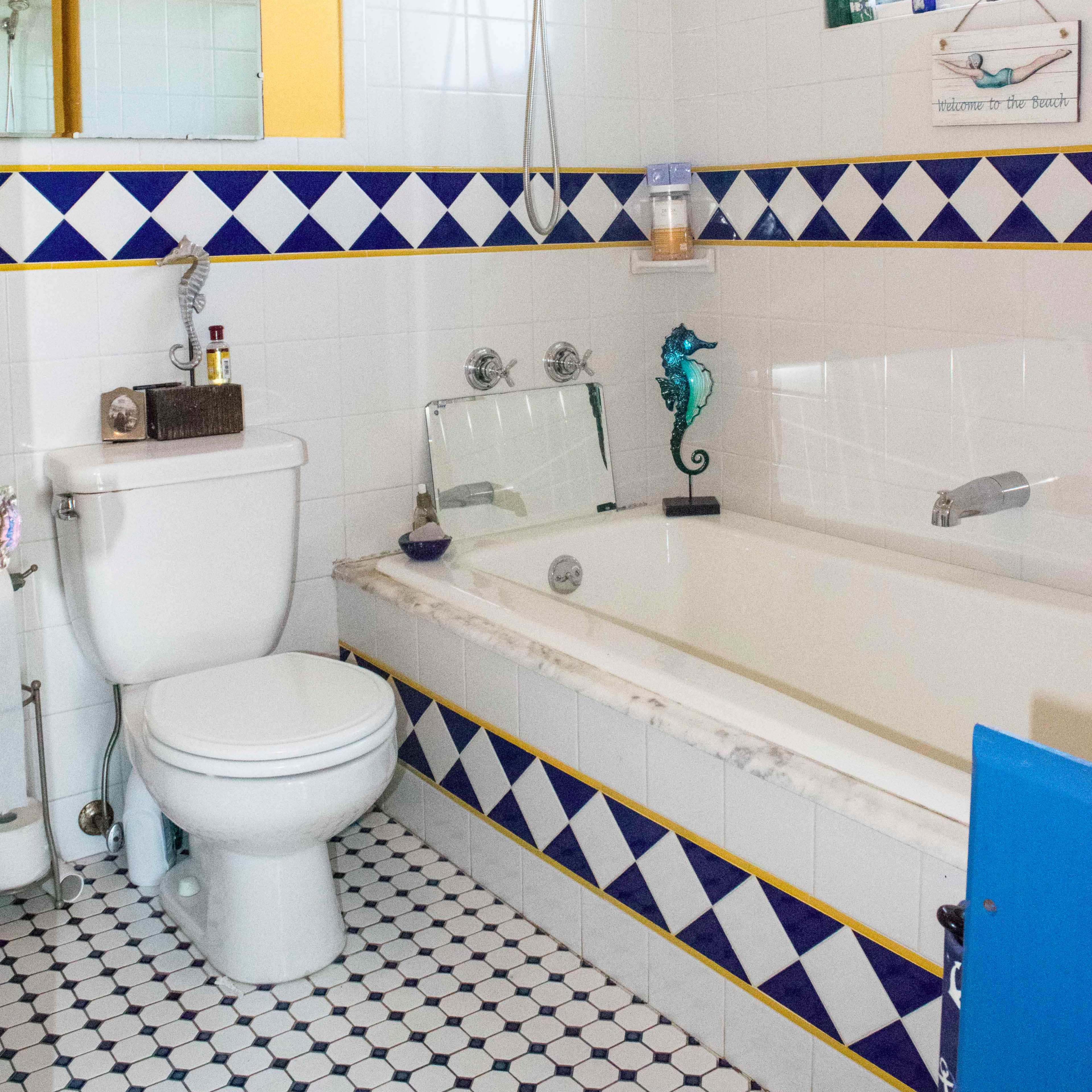 The bathroom features a bathtub with a shower head, a pedestal toilet, and colorful tile accents on the walls and floor.