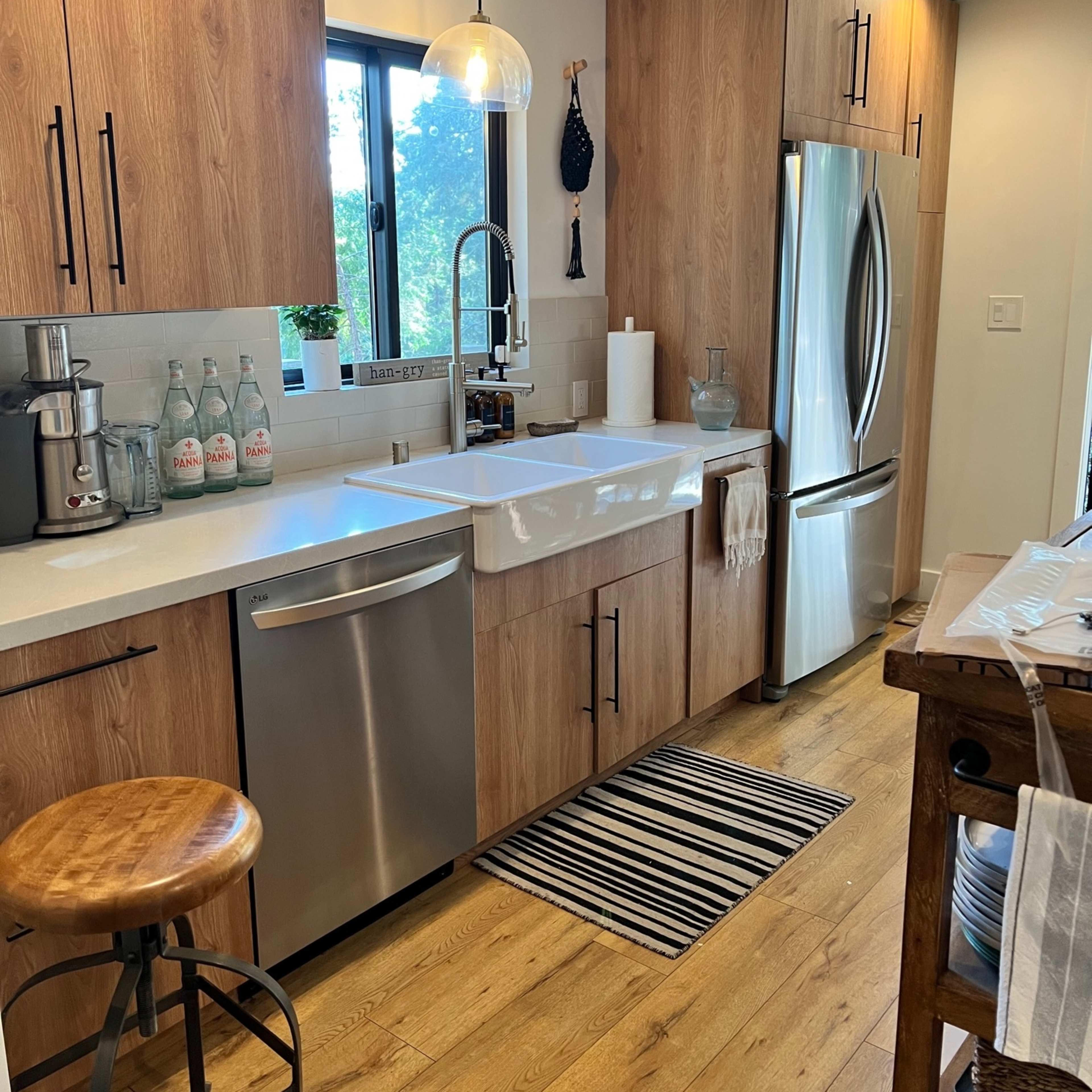 A modern kitchen features wooden cabinets, a stainless steel refrigerator, and a farmhouse sink with a window view.