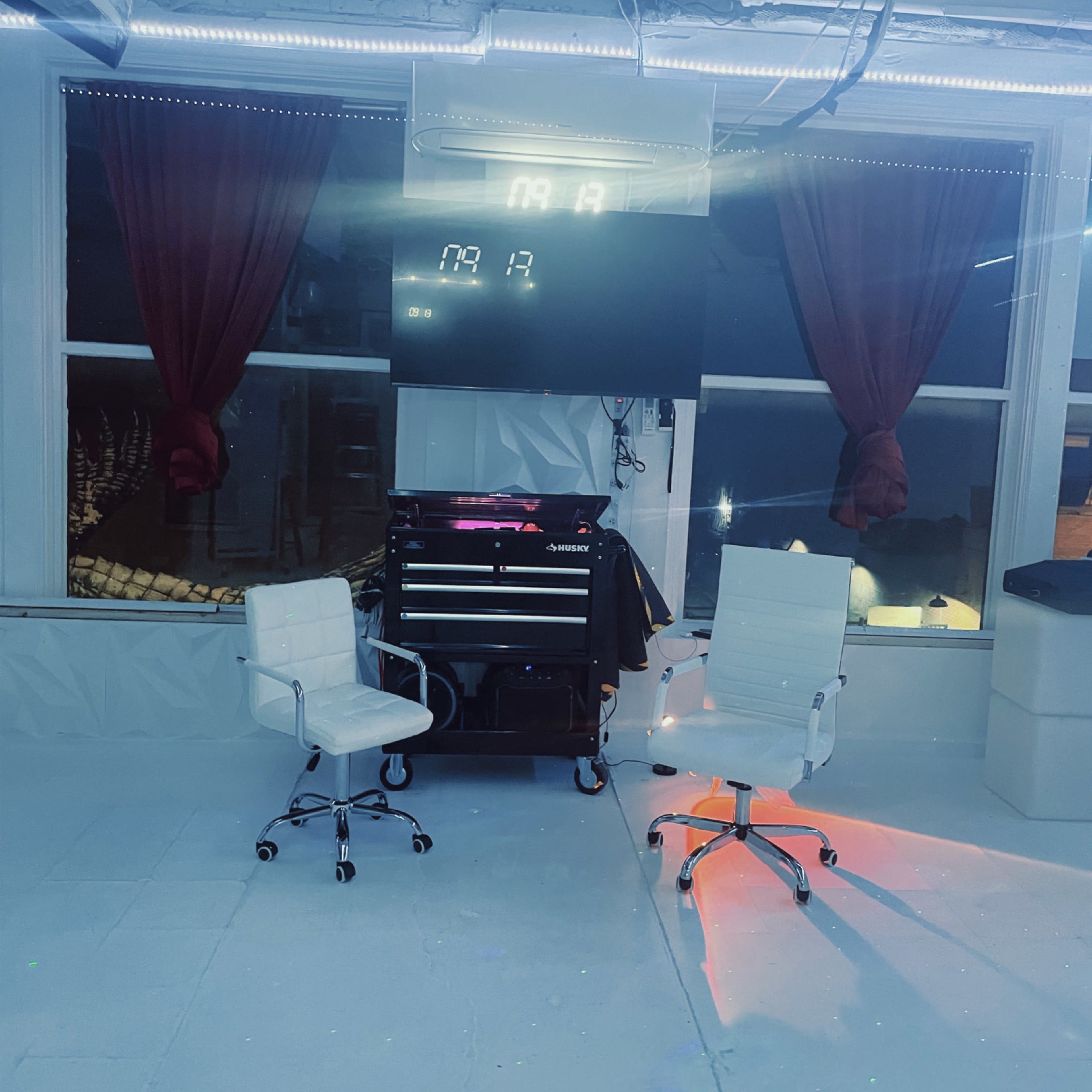 A minimalistic room with two white office chairs facing a dark display screen, flanked by red curtains and illuminated by overhead lights.