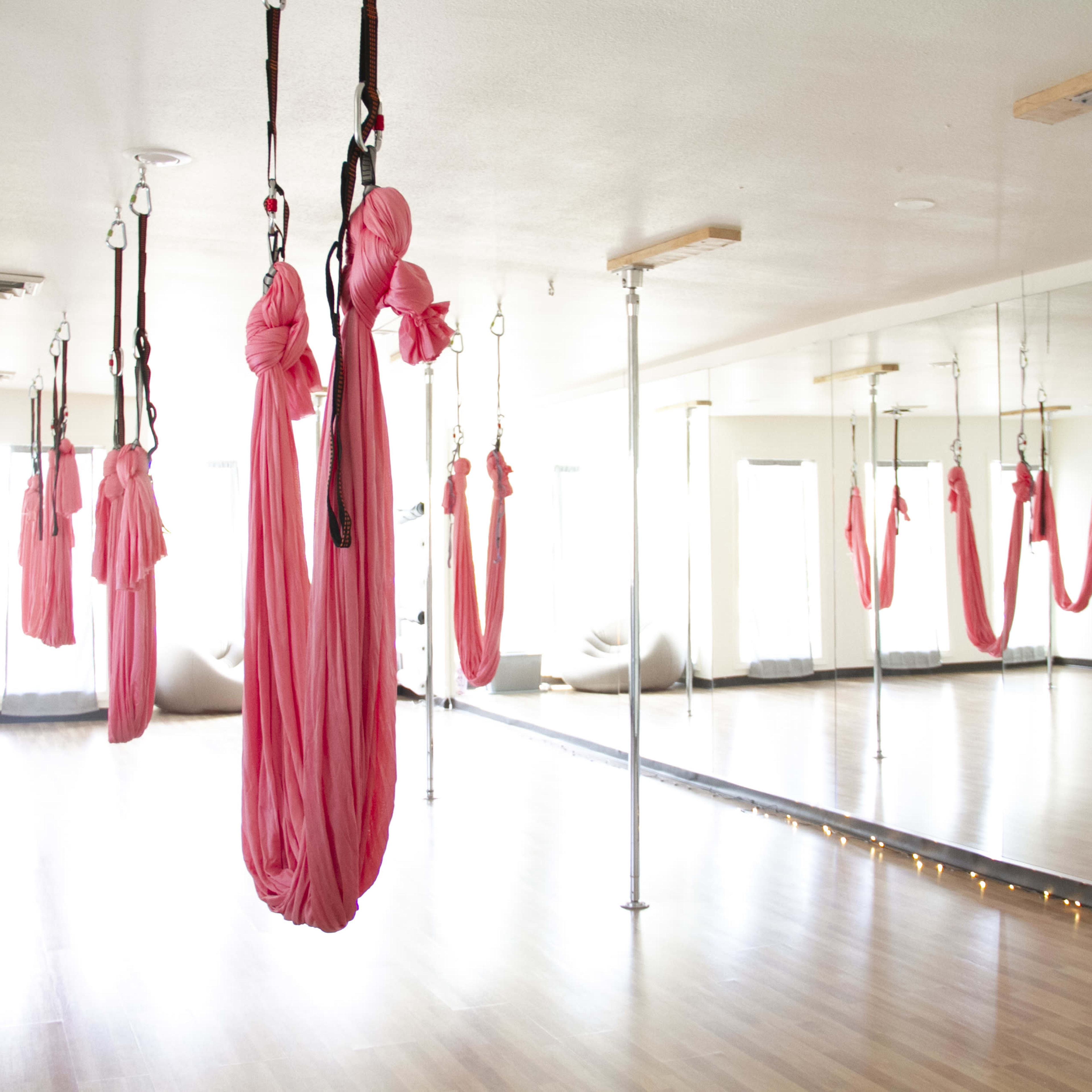 A spacious studio with bright lighting and several pink aerial hammocks suspended from the ceiling.