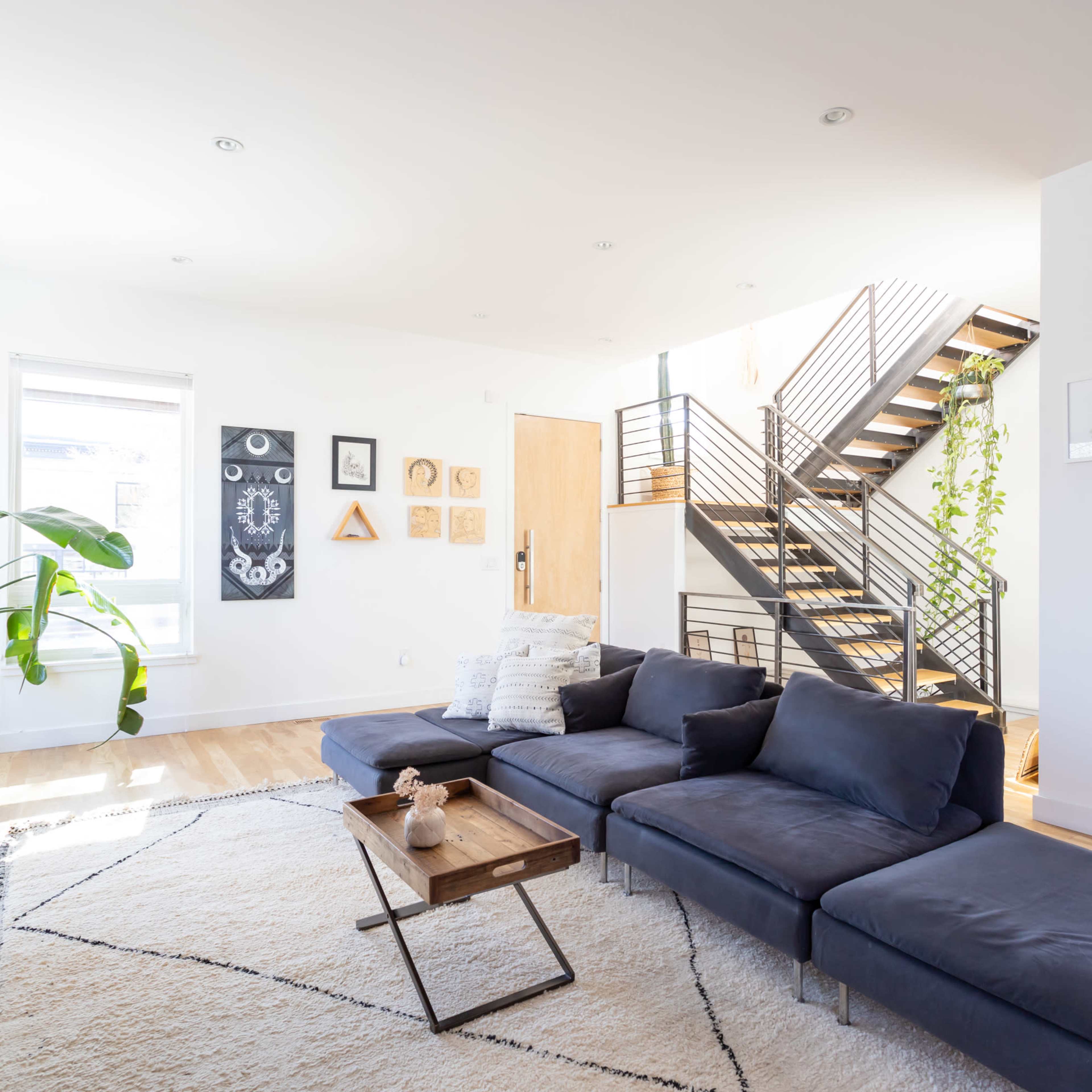 A modern living room with a dark sectional sofa, a wooden coffee table, and decorative wall art, adjacent to a staircase with metal railings.