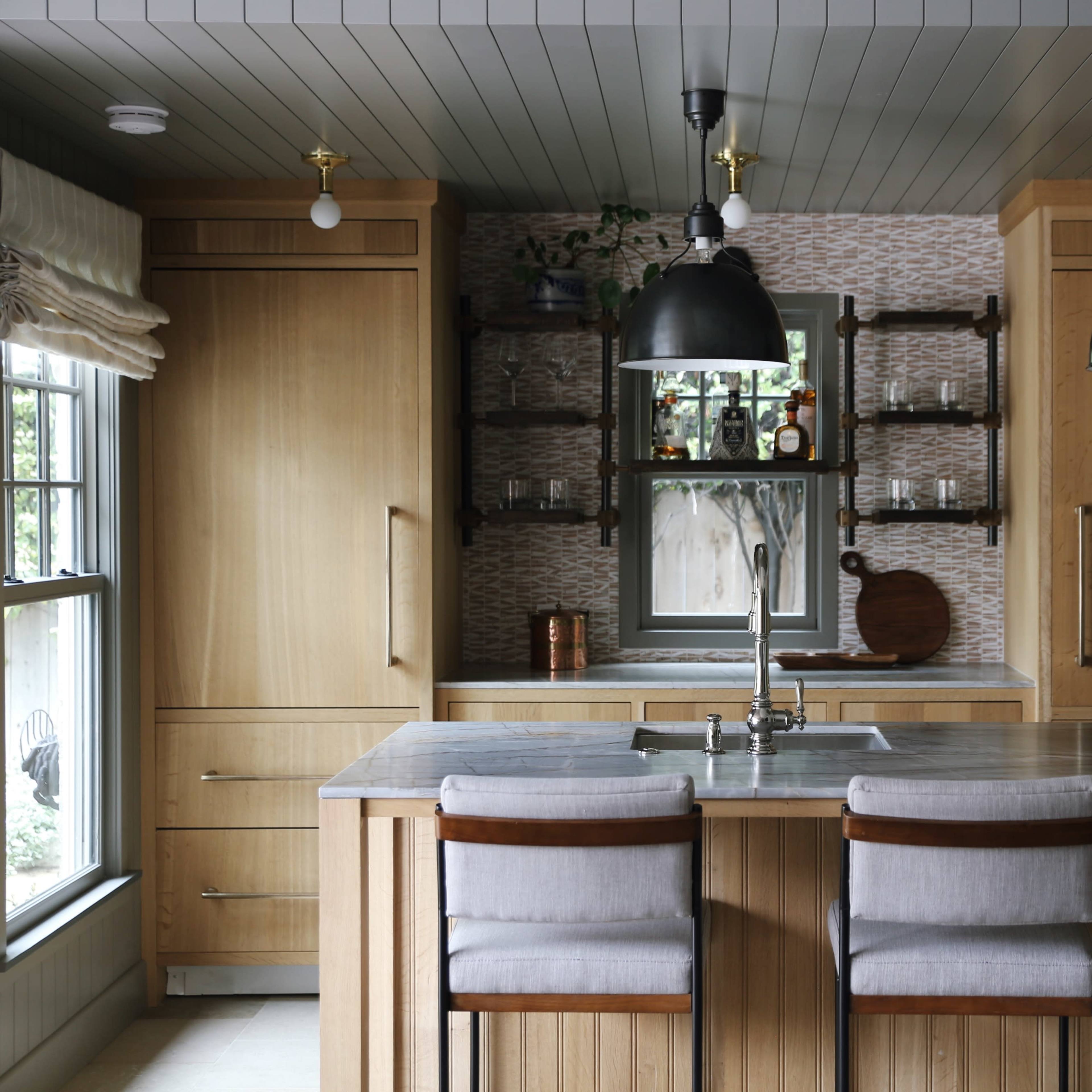 A modern kitchen with wooden cabinetry, a central island with bar stools, and pendant lighting above the sink.