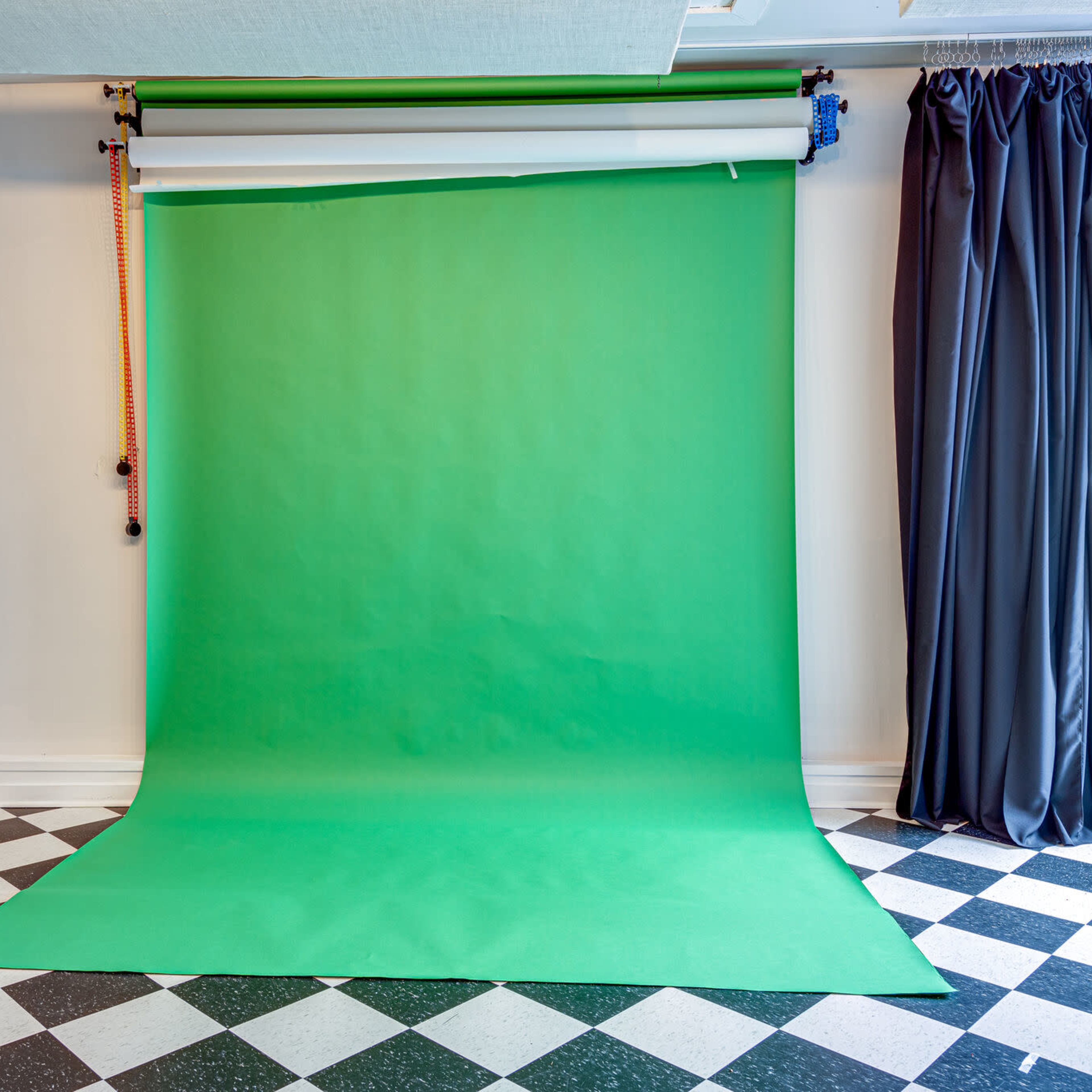 A green screen studio setup with a green backdrop and black and white checkered flooring.