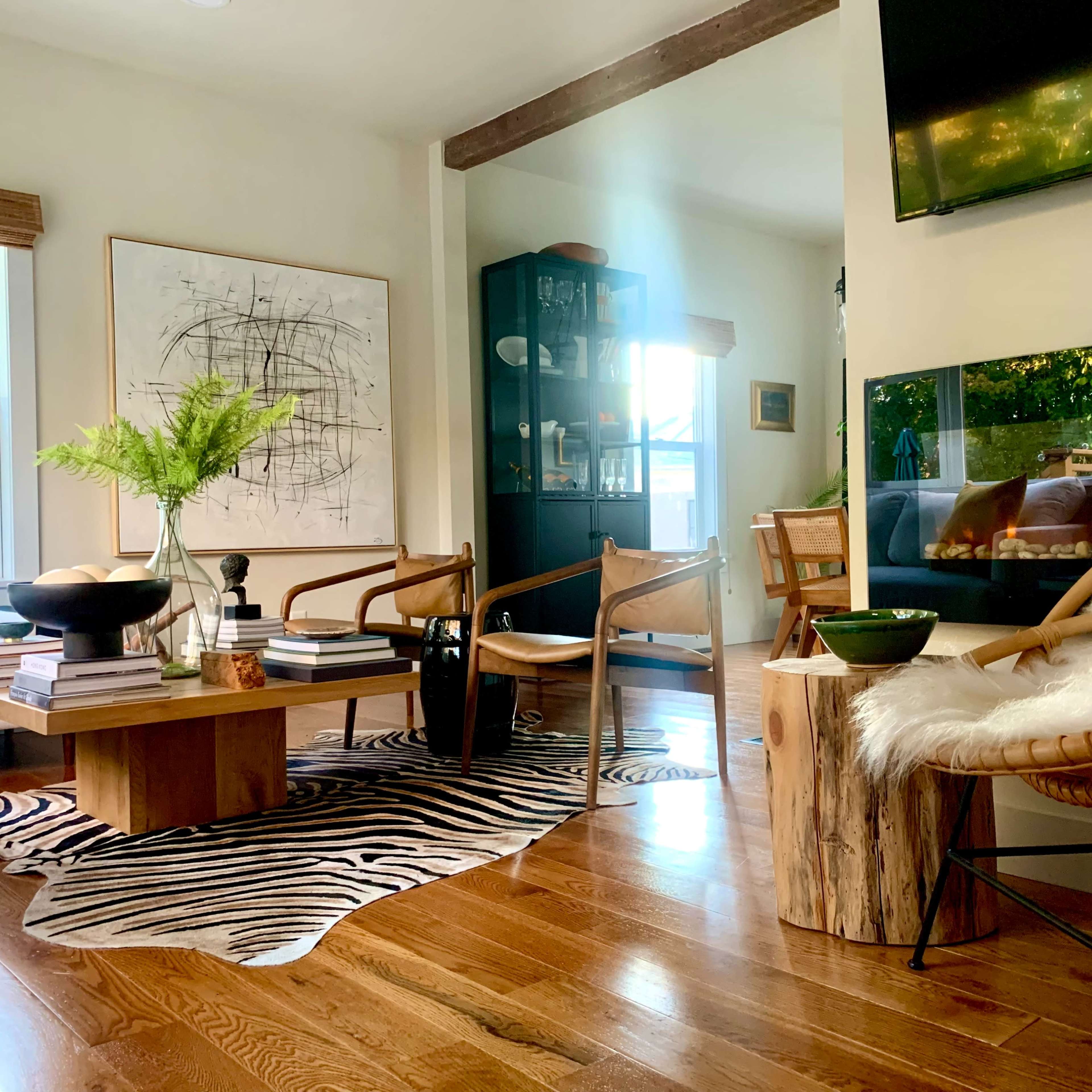 A modern living room features a wooden table, two chairs, a black display cabinet, and a television, with a zebra-patterned rug on the floor.