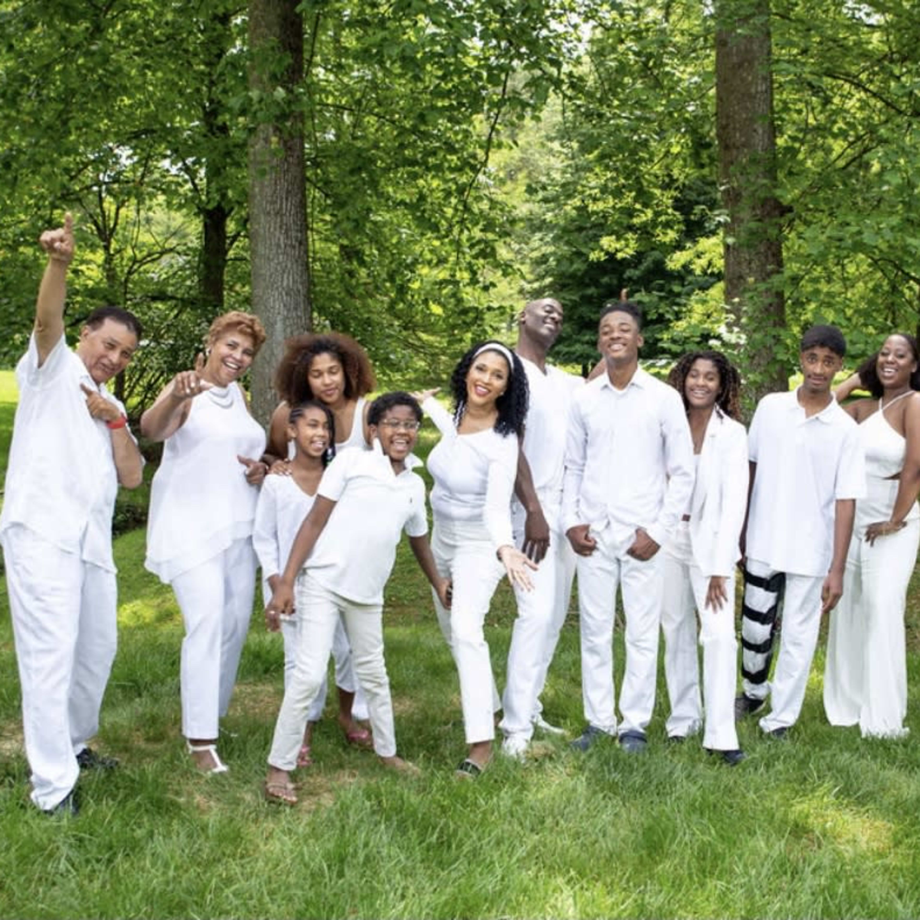 A group of people dressed in white clothing stands together in a green outdoor setting, smiling and posing for a photo.