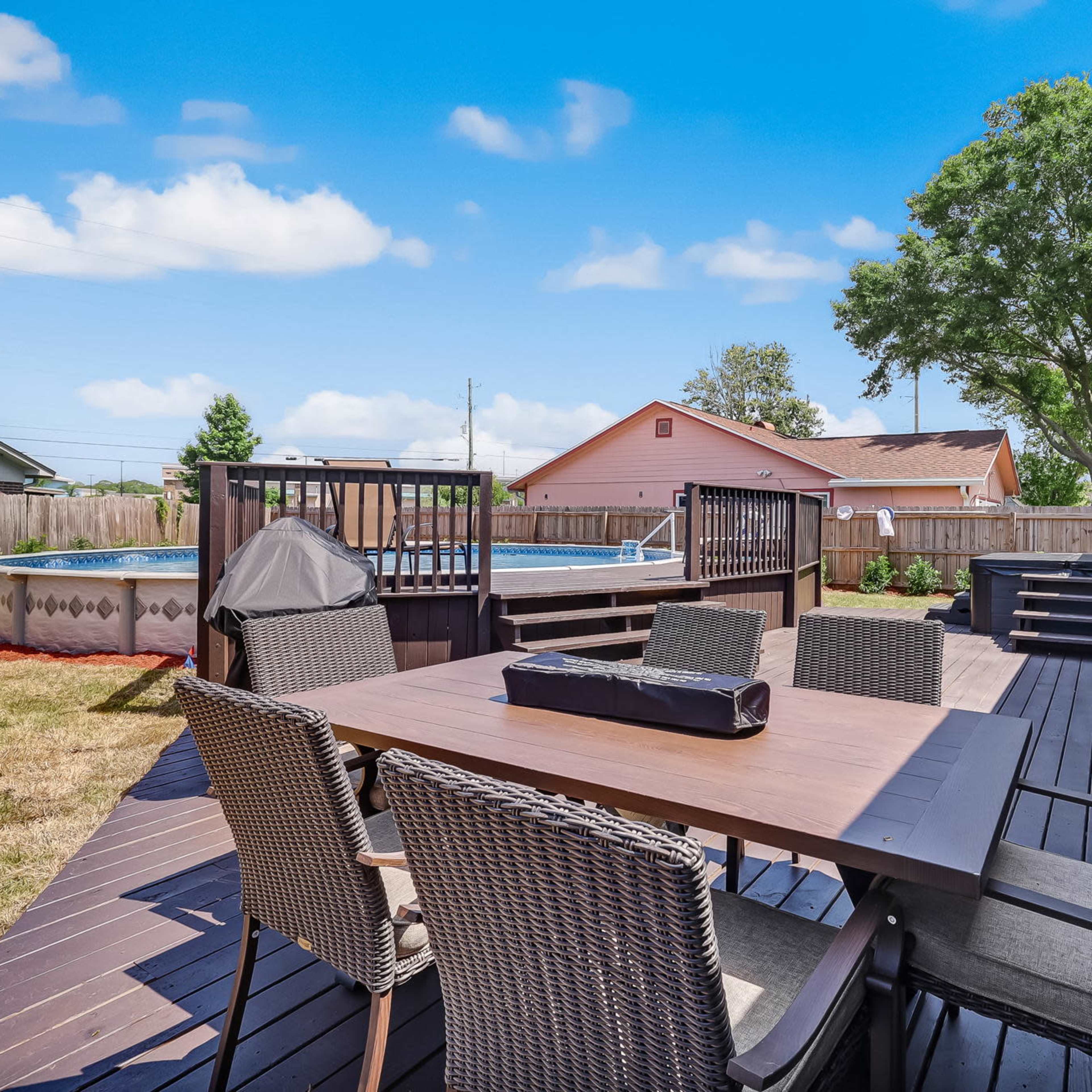 A well-furnished deck with a dining table, surrounded by chairs, a hot tub, and a swimming pool in the backyard.