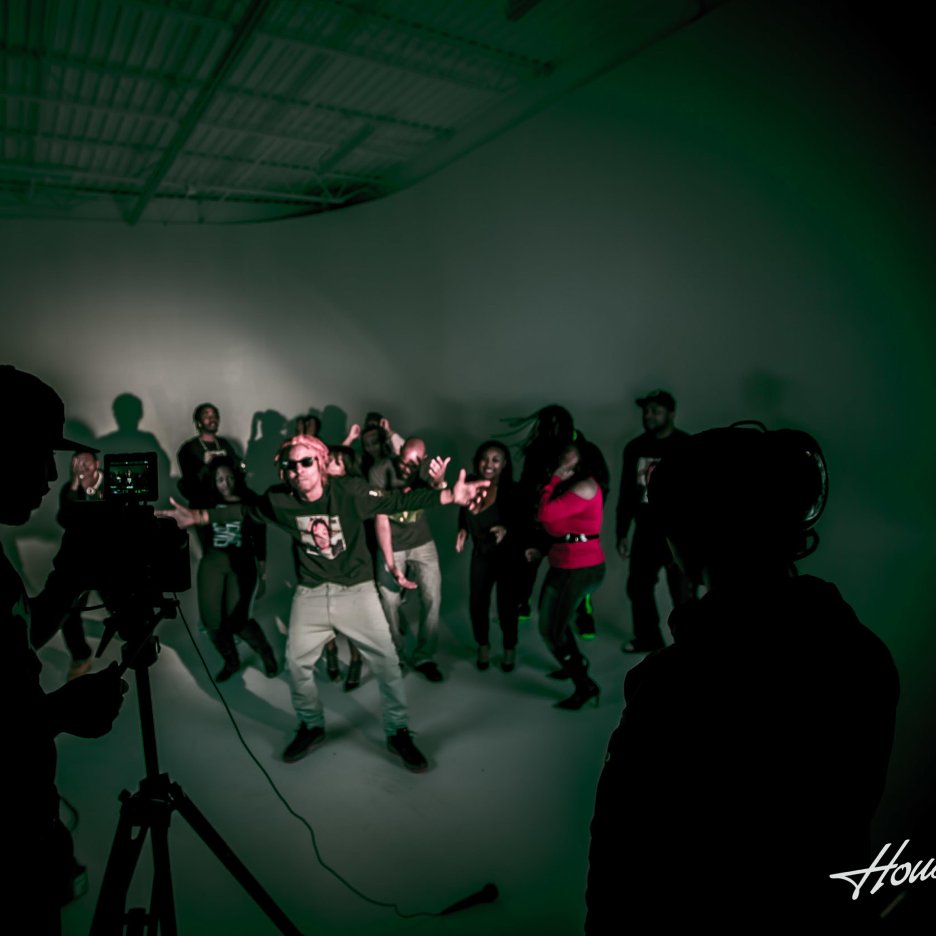 A group of people is dancing in a studio, while cameras and equipment are set up in the foreground.