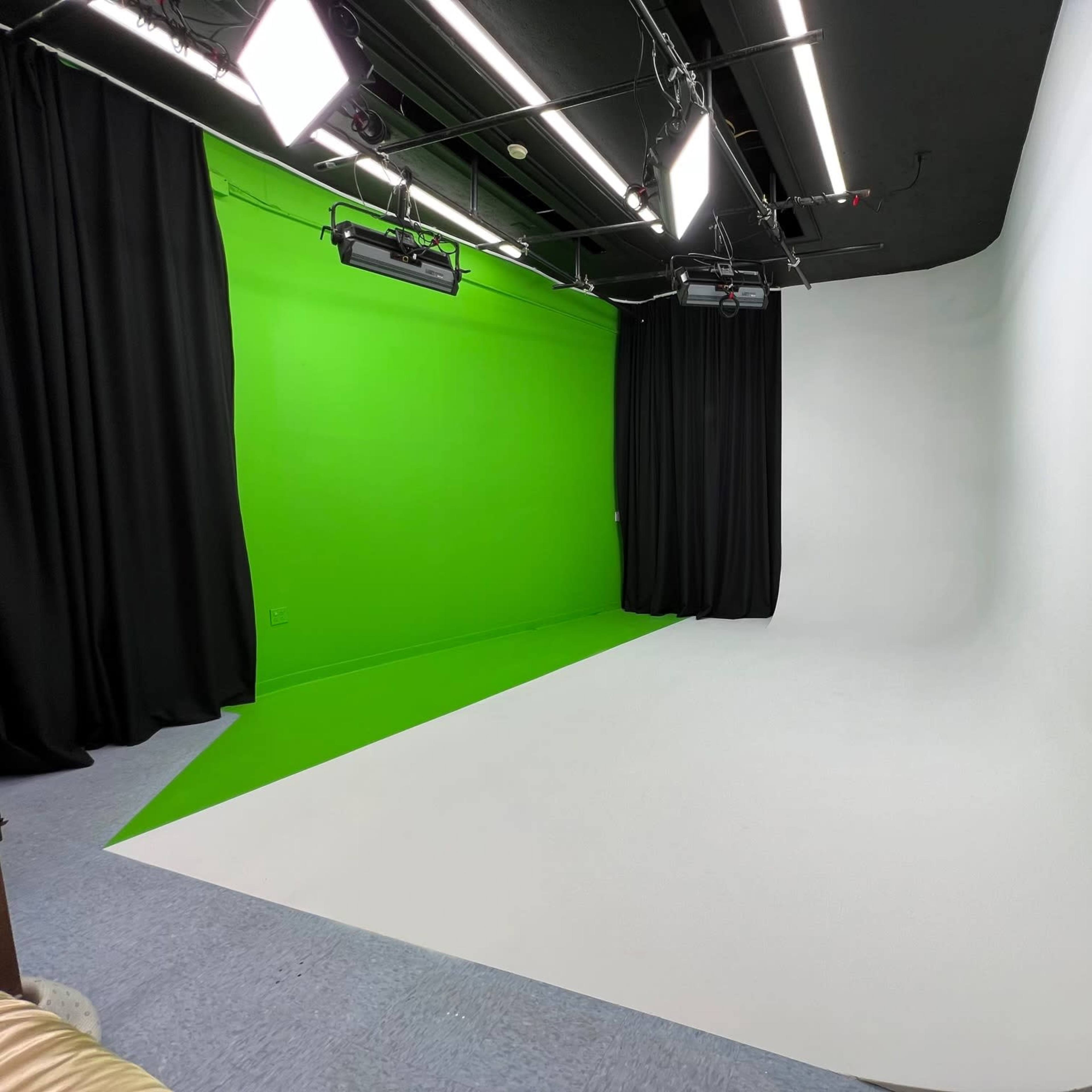A photography studio featuring a green screen on one side and a white seamless backdrop on the other, with lights and curtains around the space.