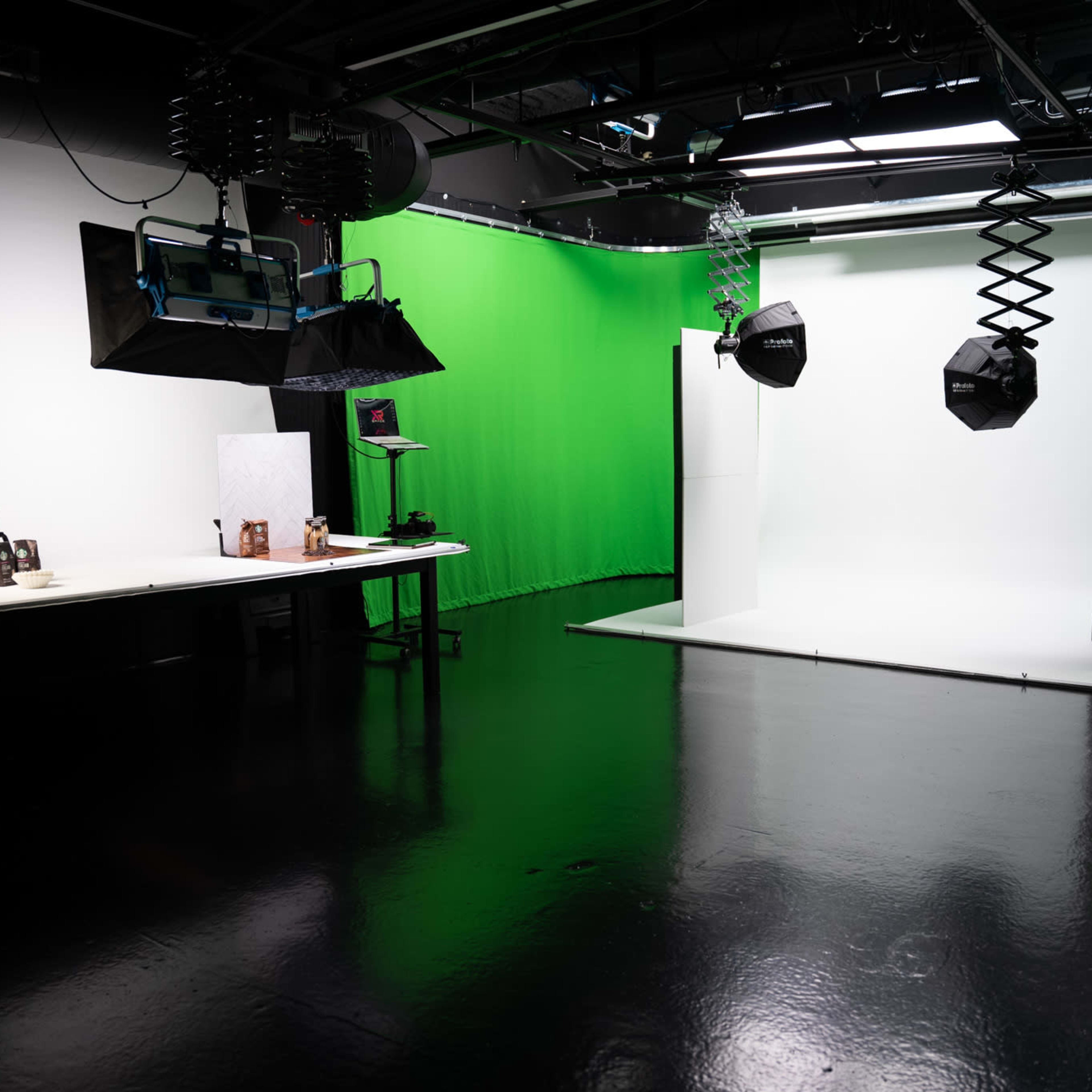 A photography studio features a green backdrop, a white backdrop, and various lighting equipment on a reflective floor.