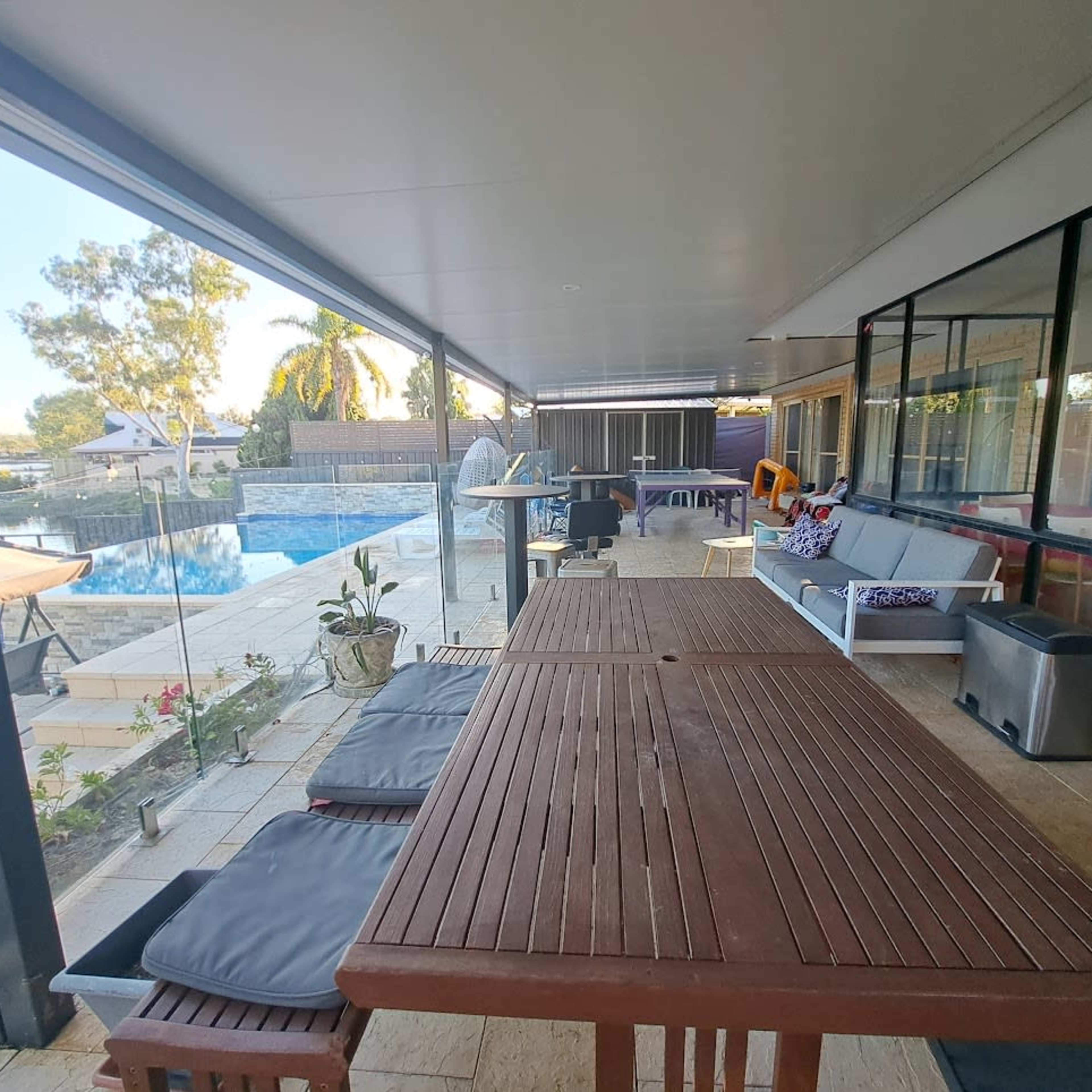 A spacious outdoor patio with a wooden table and chairs, overlooking a pool surrounded by landscaped areas.
