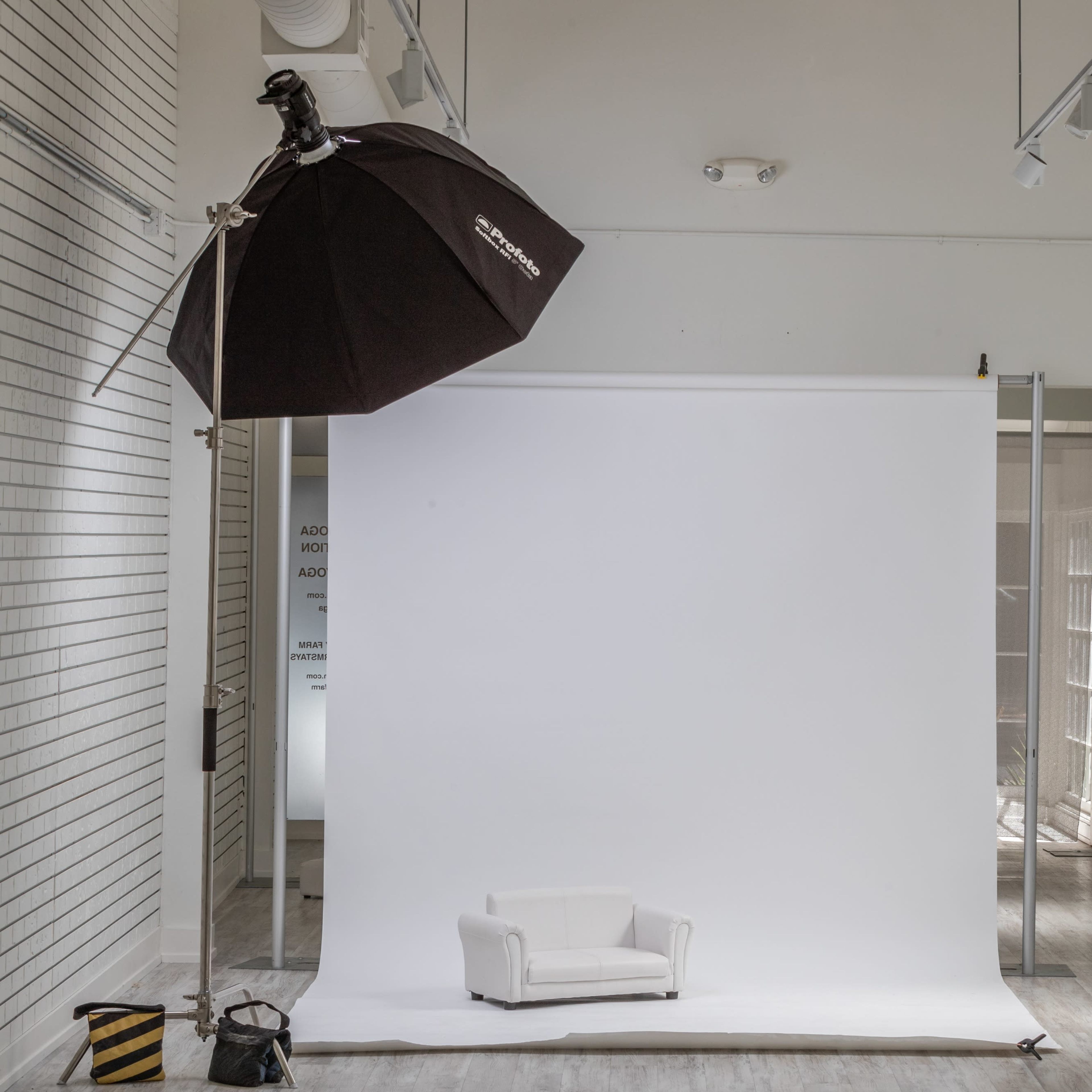 A minimalist photography studio with a white backdrop, a small white couch, and a large softbox light setup.