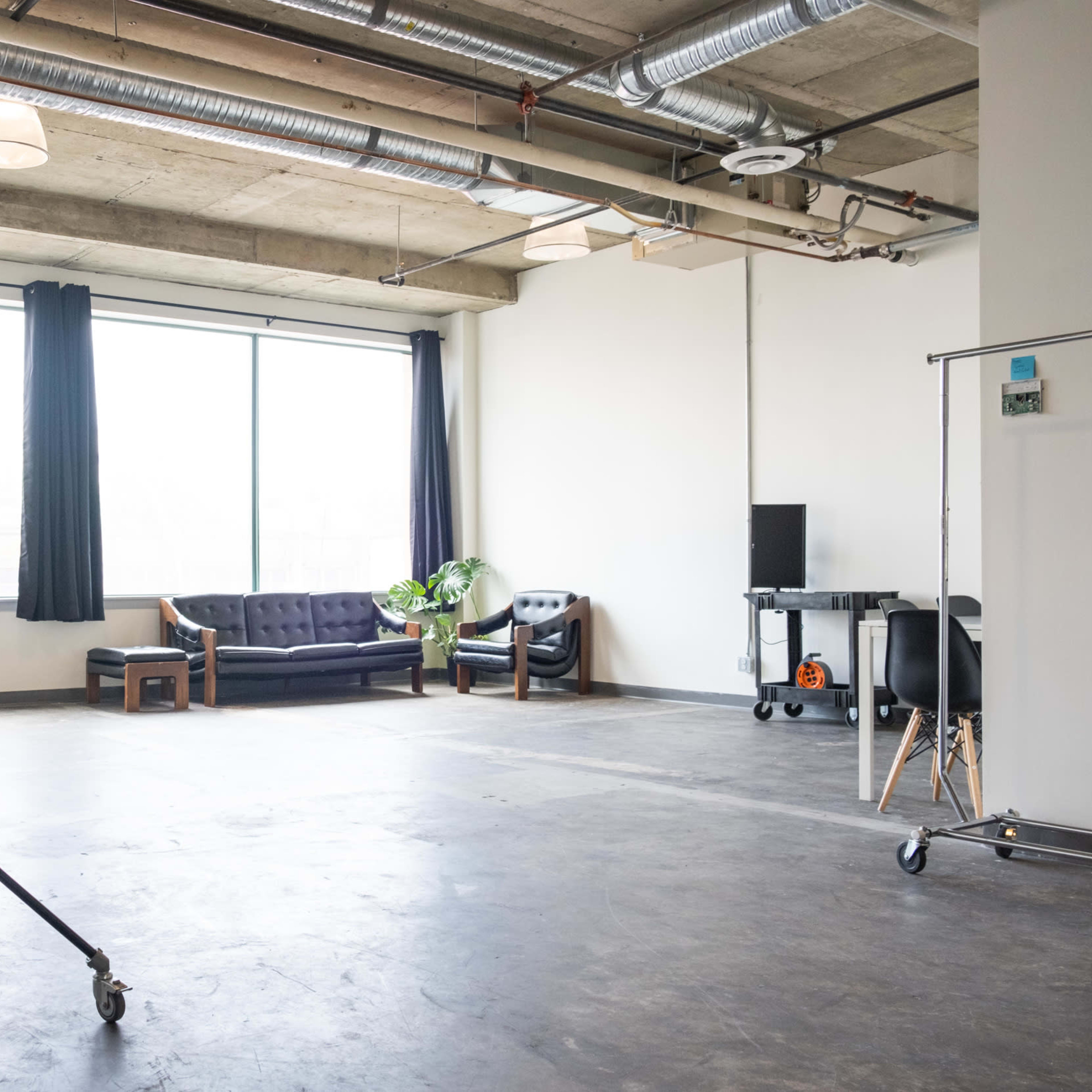 A spacious room with large windows, featuring a sofa, armchairs, and studio equipment.