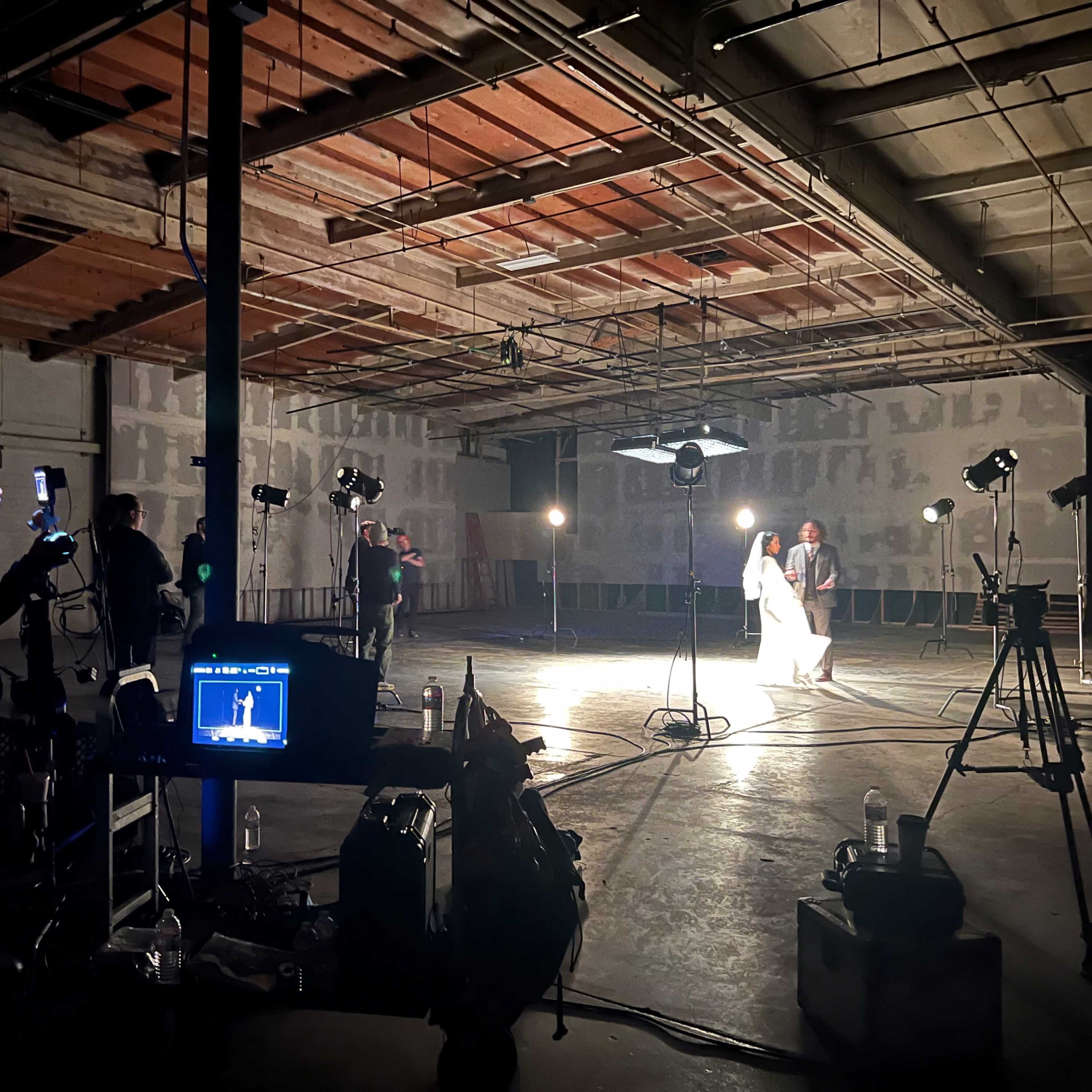 A film crew sets up lights and equipment in a spacious, partially finished warehouse for a photo shoot.