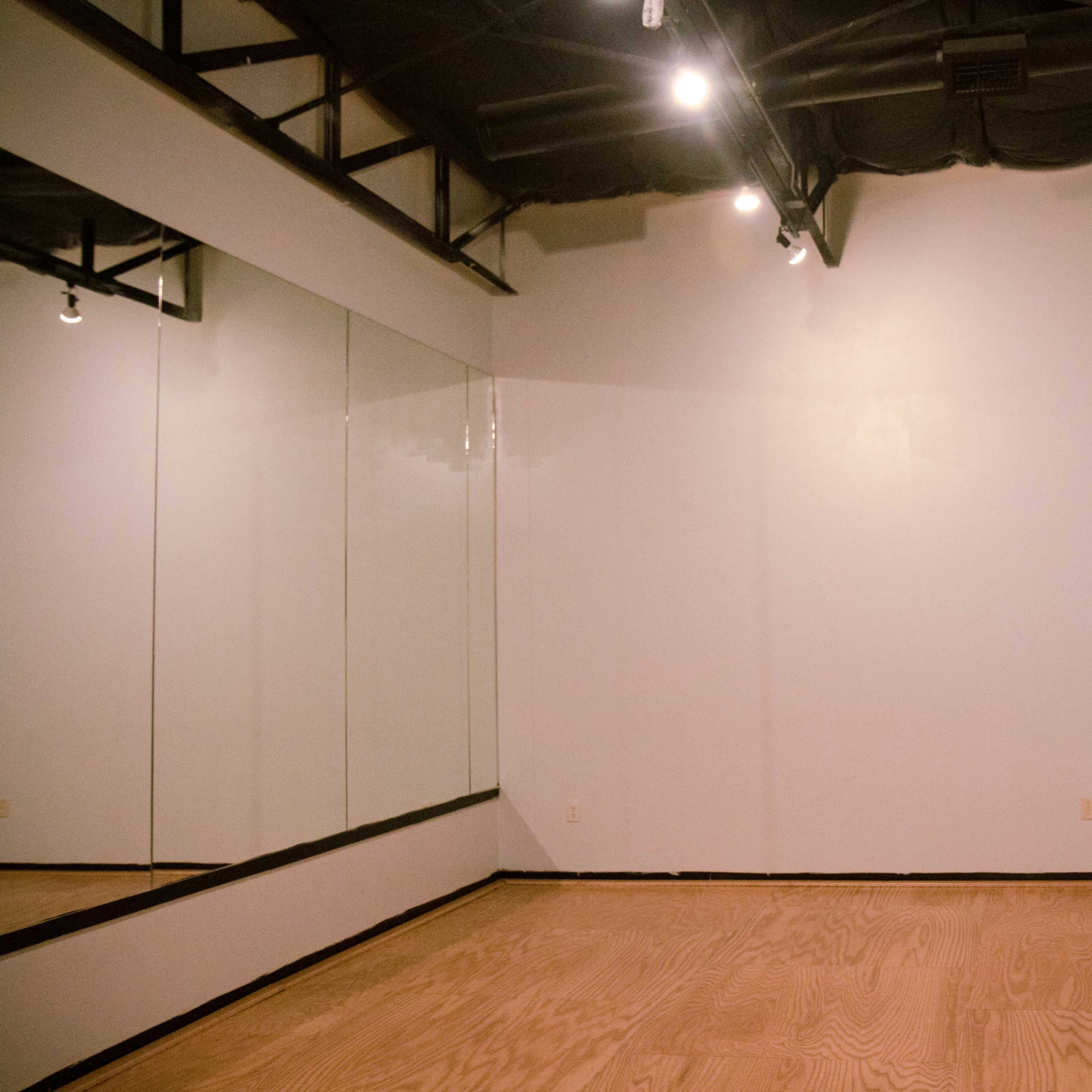A spacious dance studio with wooden flooring, a wall-mounted ballet bar, and a large mirror.