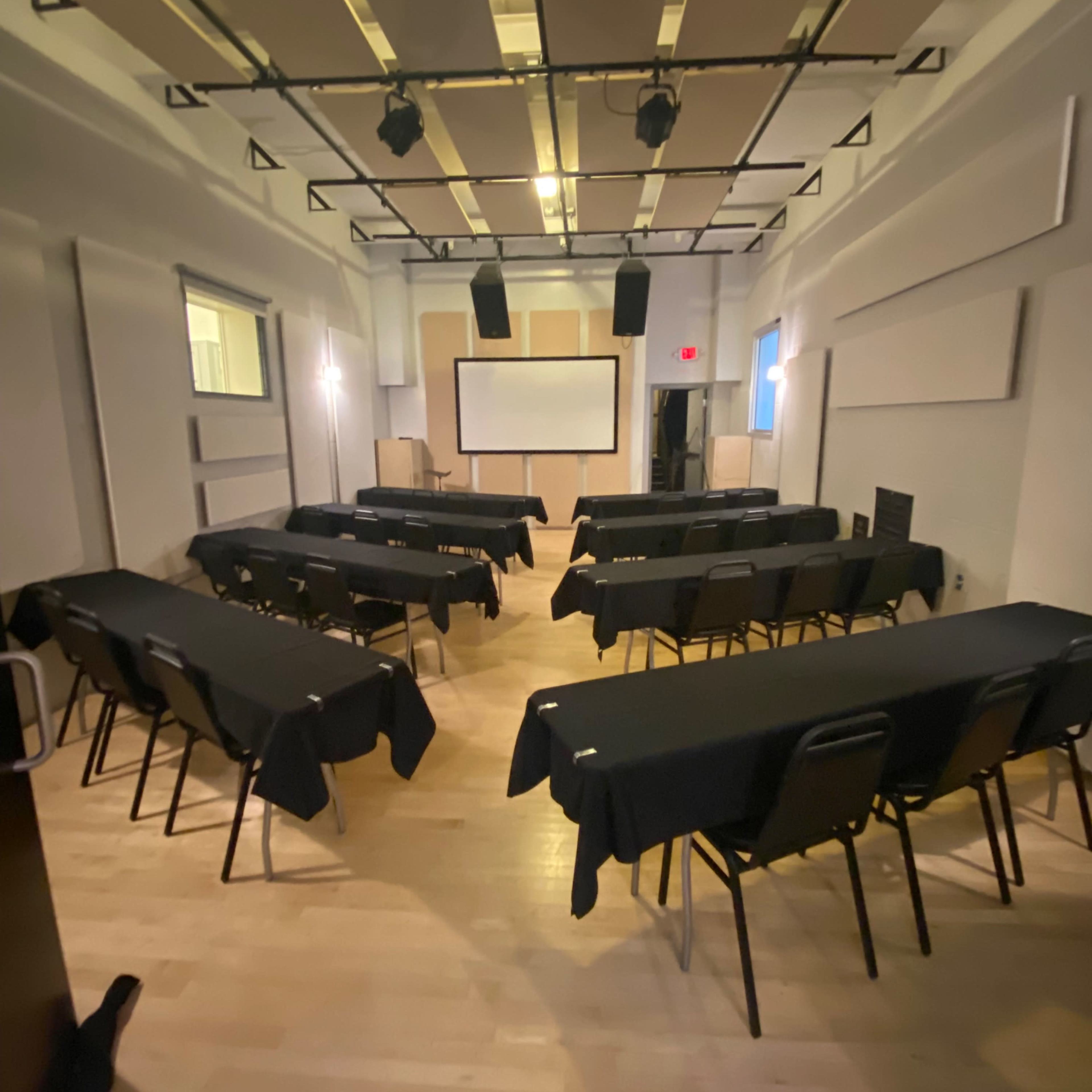 A conference room is set up with rows of tables covered in black cloth and chairs arranged for a presentation.