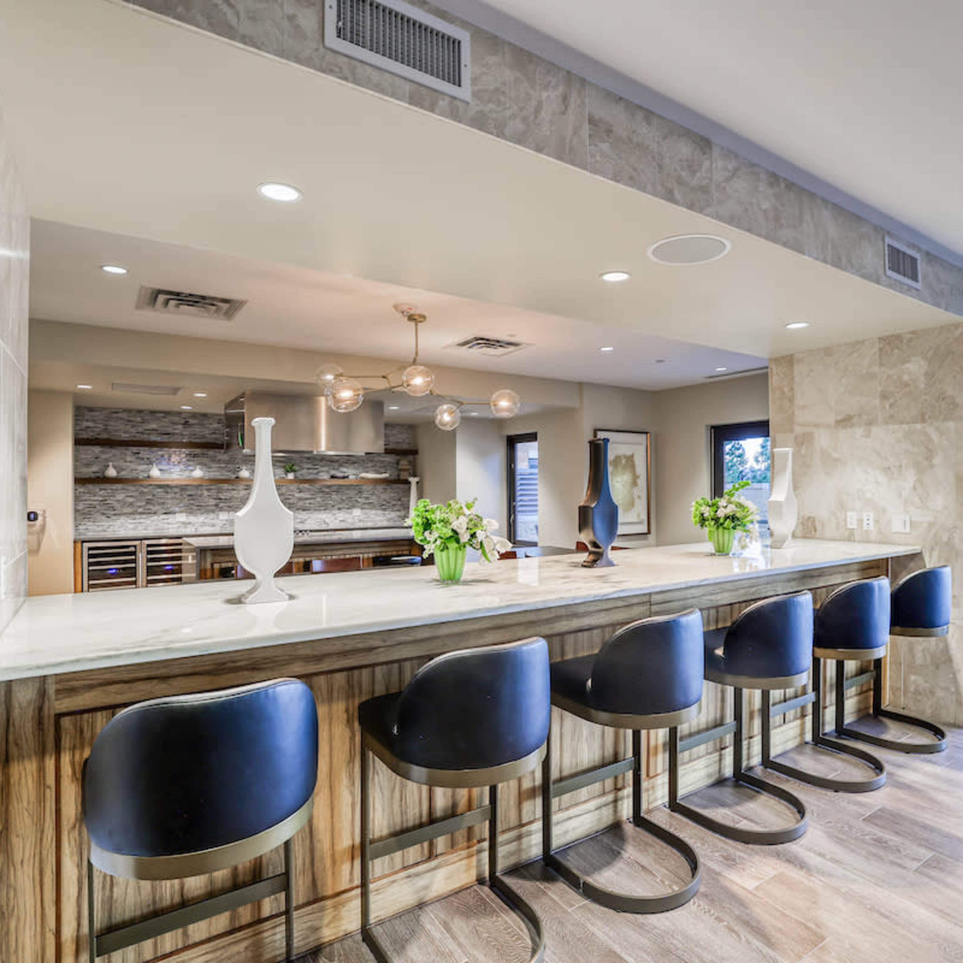 A modern kitchen with a large island bar featuring black stools, surrounded by light-colored cabinetry and a spacious layout.