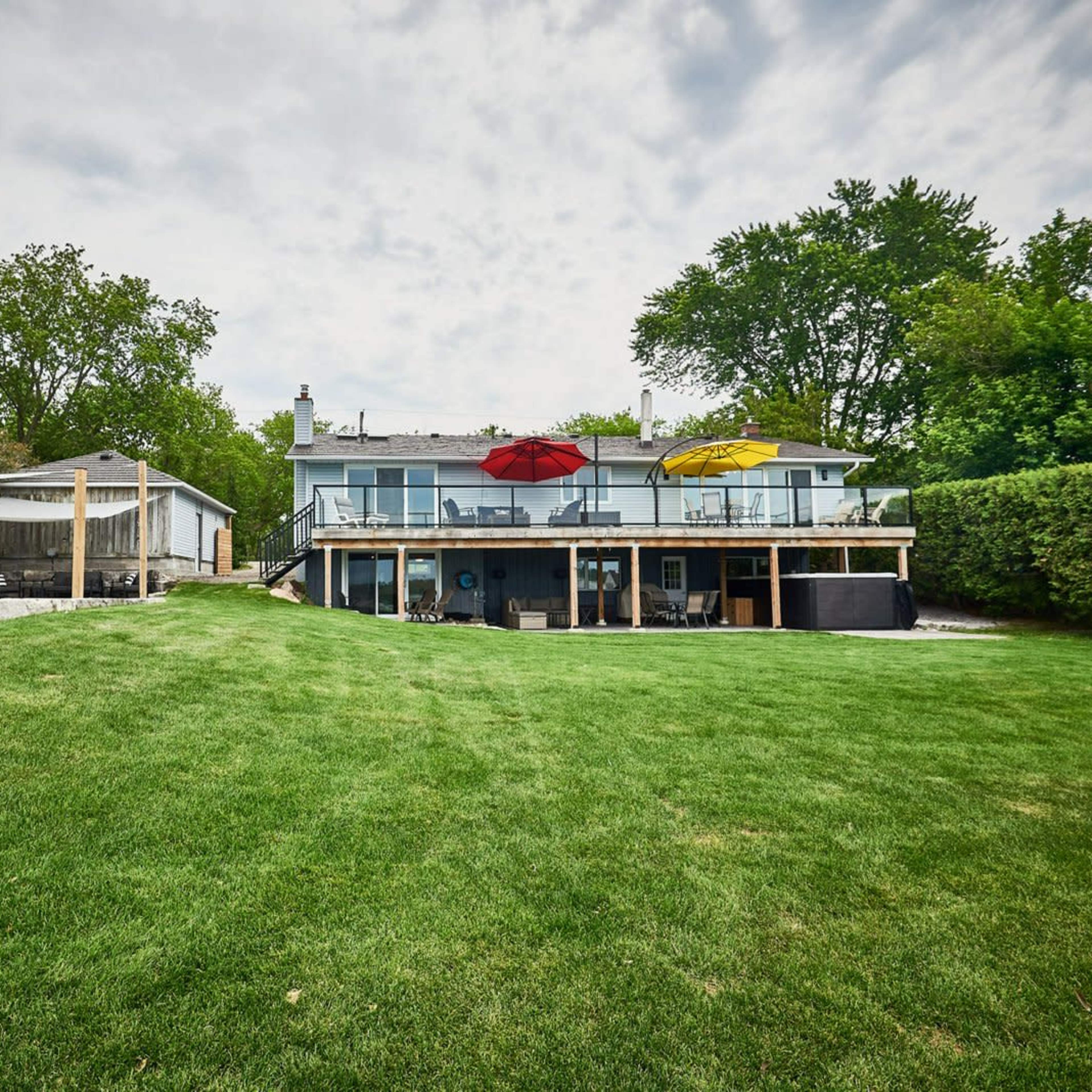 A spacious backyard with a well-maintained lawn, a two-story house featuring upper decks with red and yellow umbrellas, and a small outbuilding nearby.