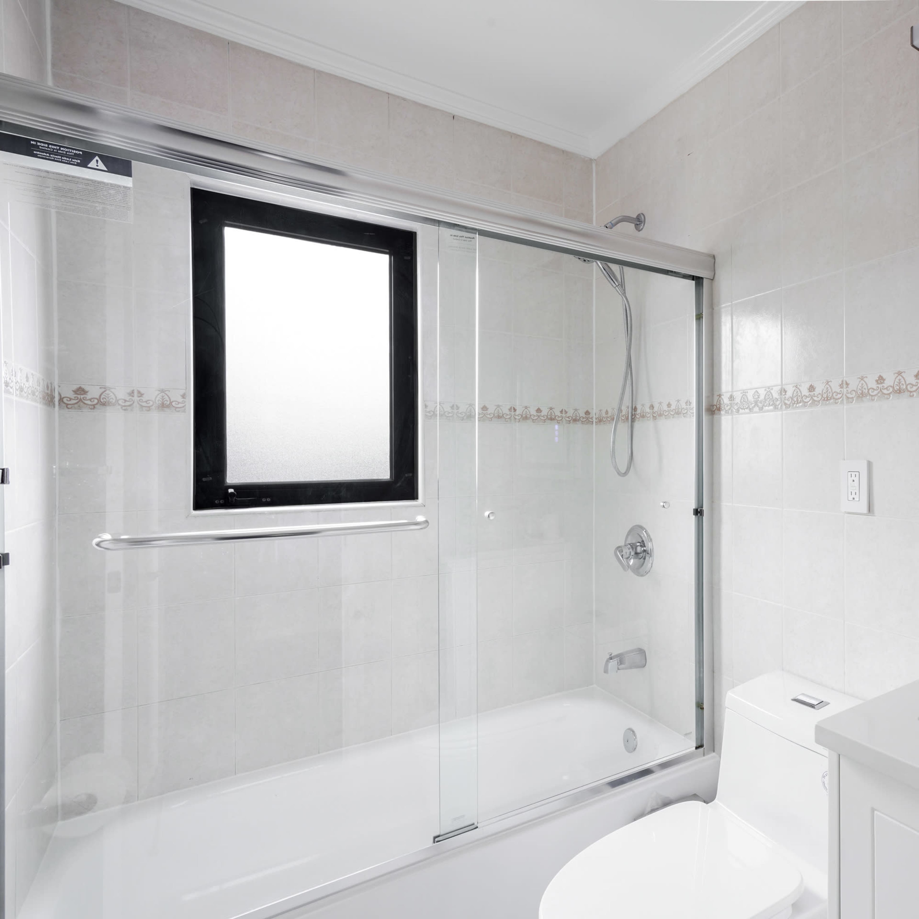 A modern bathroom featuring a glass-enclosed shower, a bathtub, a white vanity with a mirror, and a window.