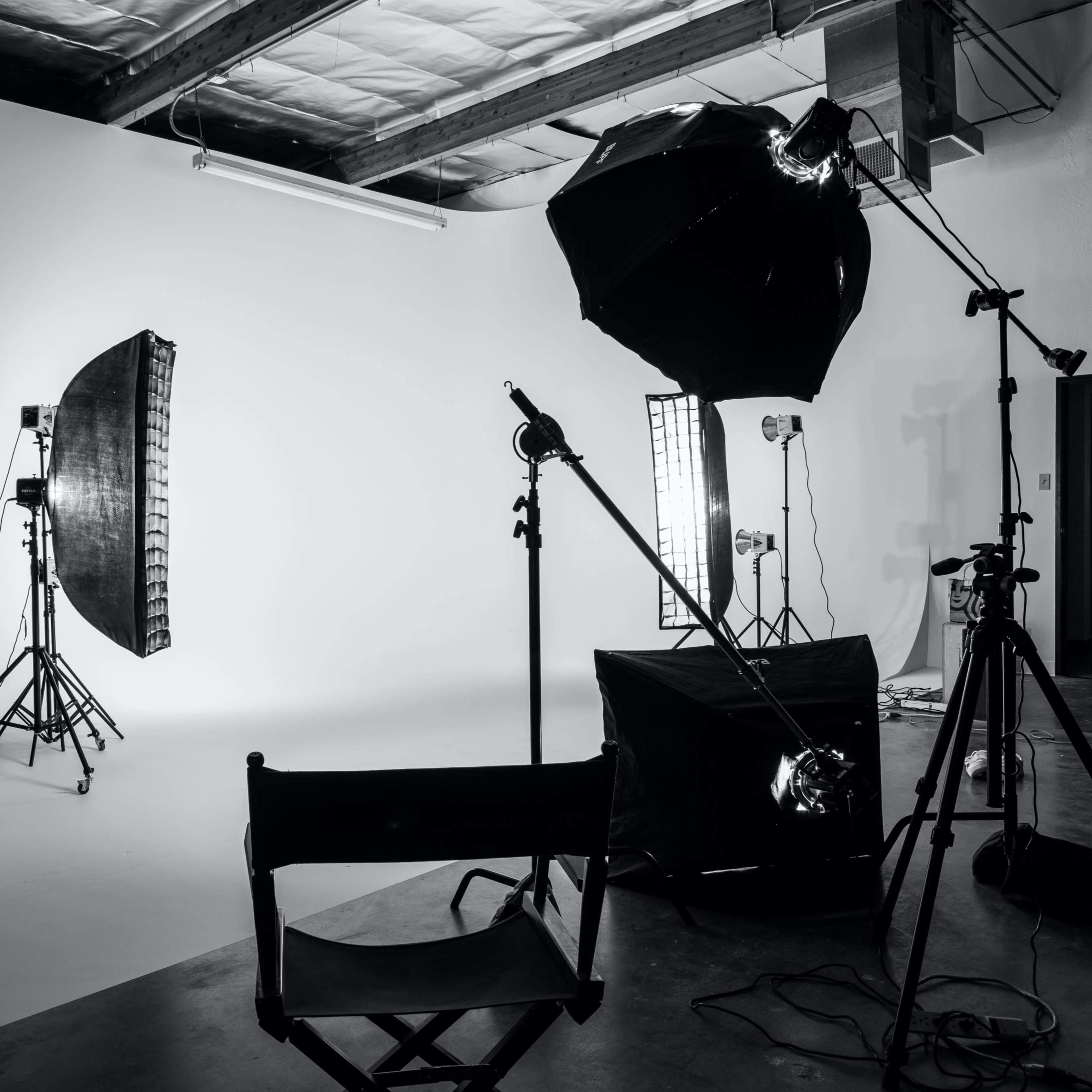 An empty photography studio setup with various lighting equipment and a director's chair positioned in front of a plain backdrop.