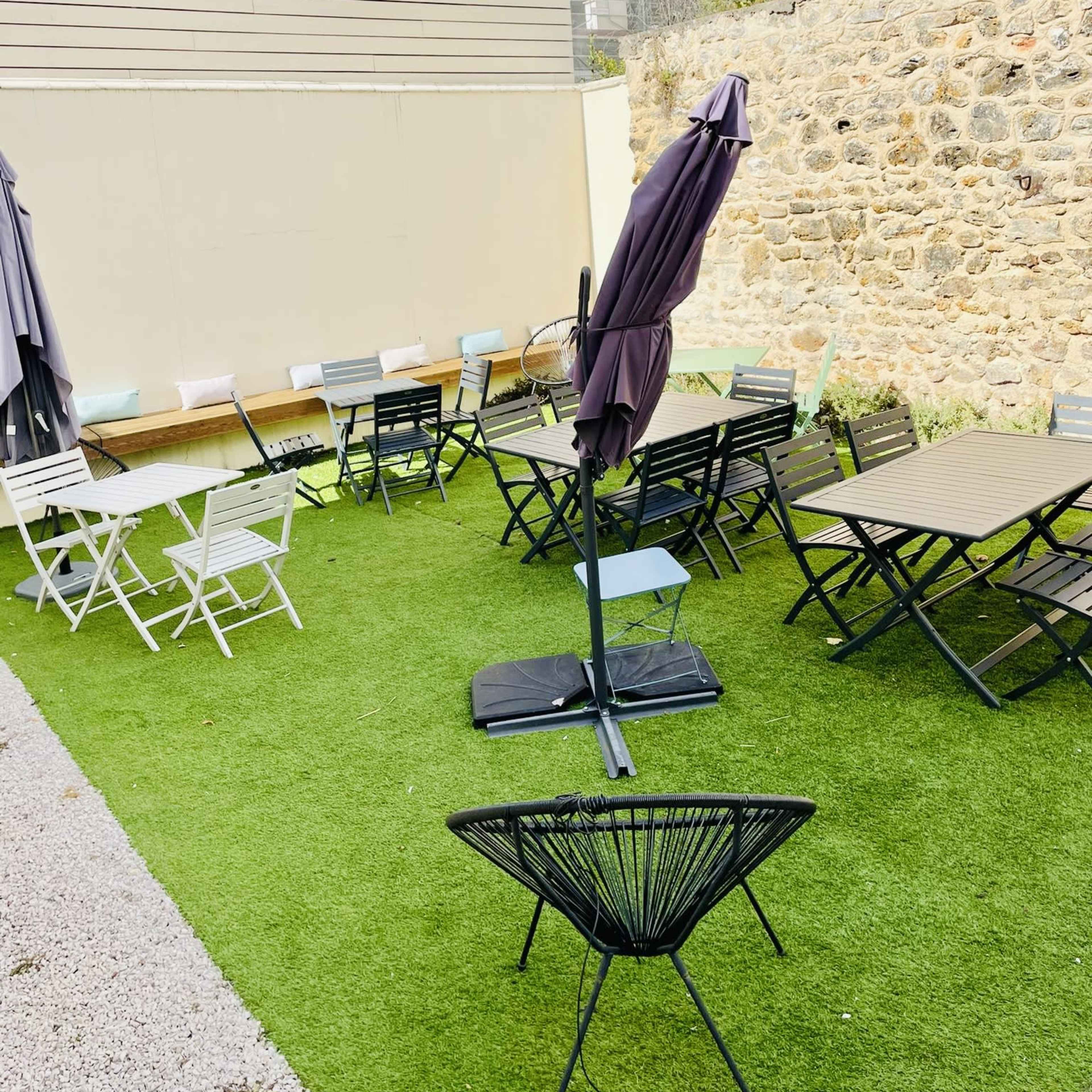 An outdoor seating area featuring various tables and chairs on artificial grass, along with several umbrellas.