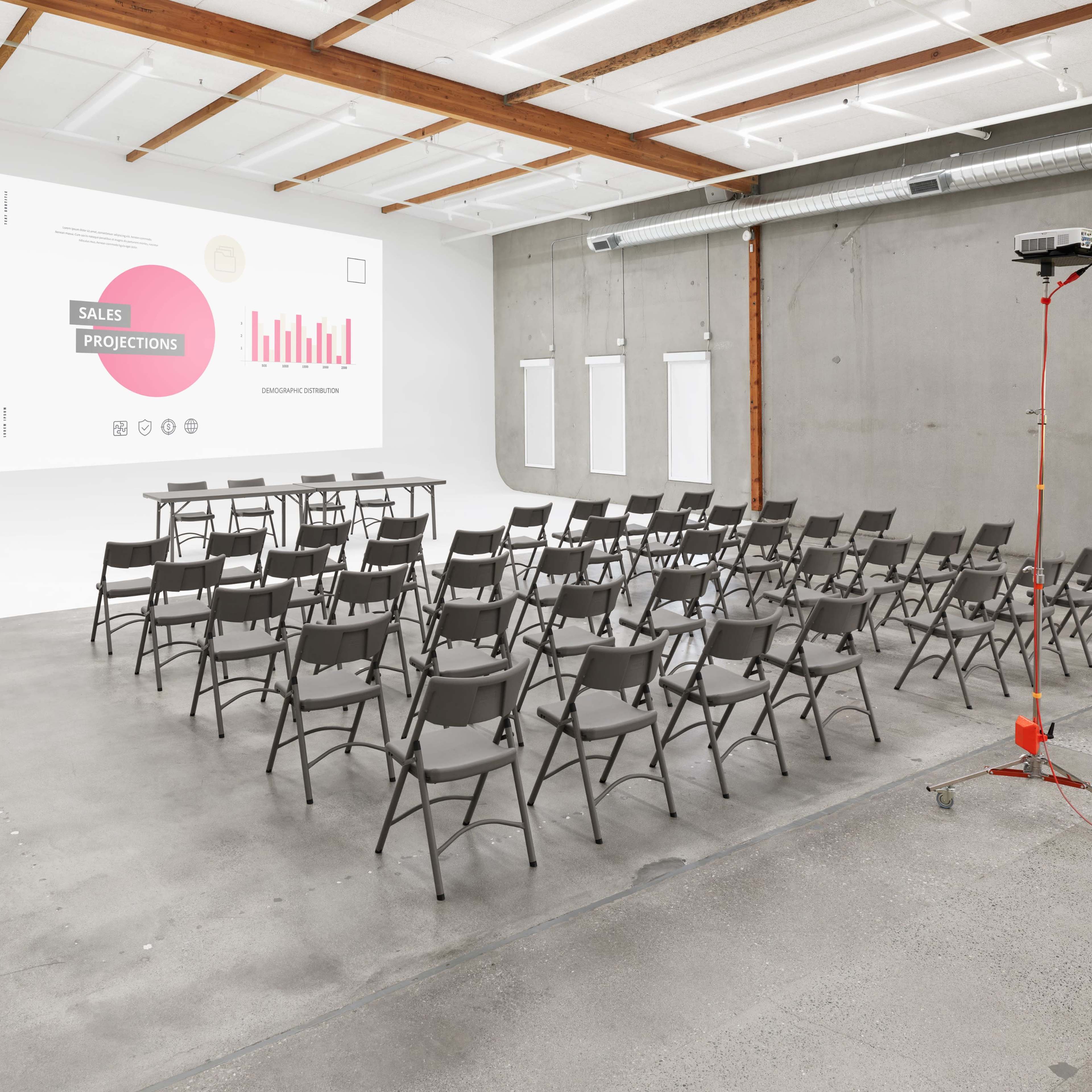A conference room features rows of gray chairs facing a blank wall with a large projector screen displaying sales projections.