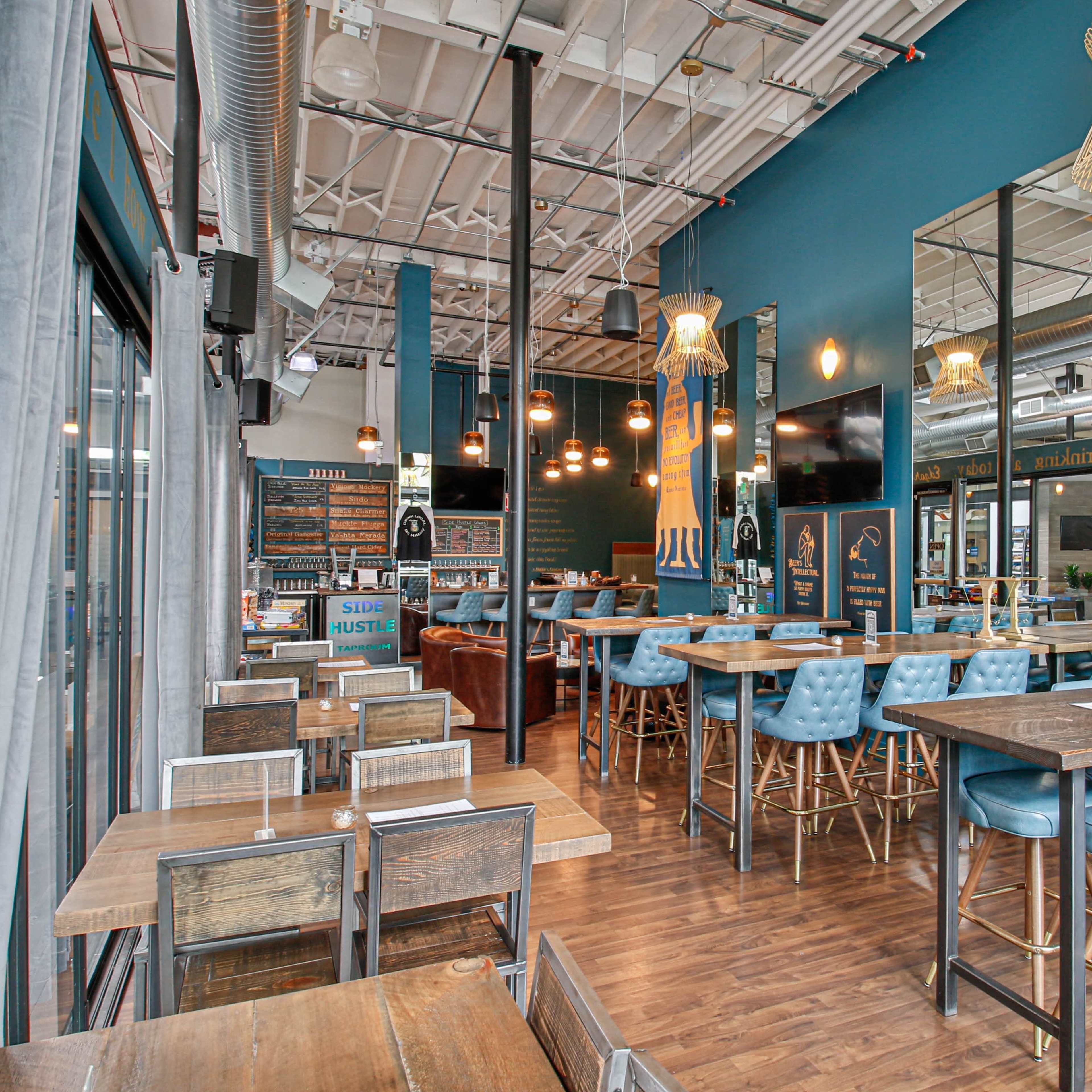 A modern bar interior with blue walls, wooden tables, and blue upholstered seating, featuring large mirrors and soft lighting.