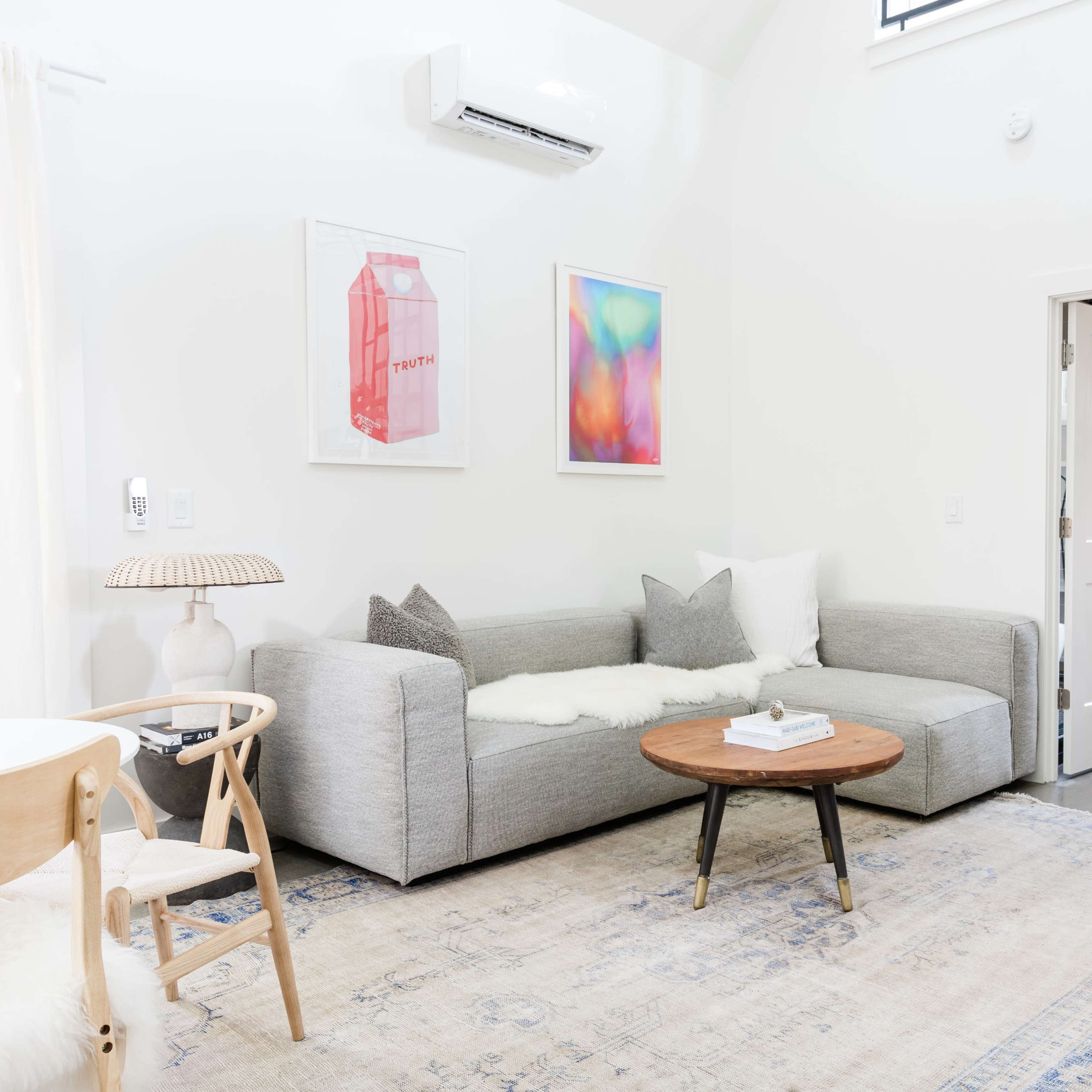A modern living room featuring a grey sectional sofa, a round wooden coffee table, and a large plant beside a staircase.