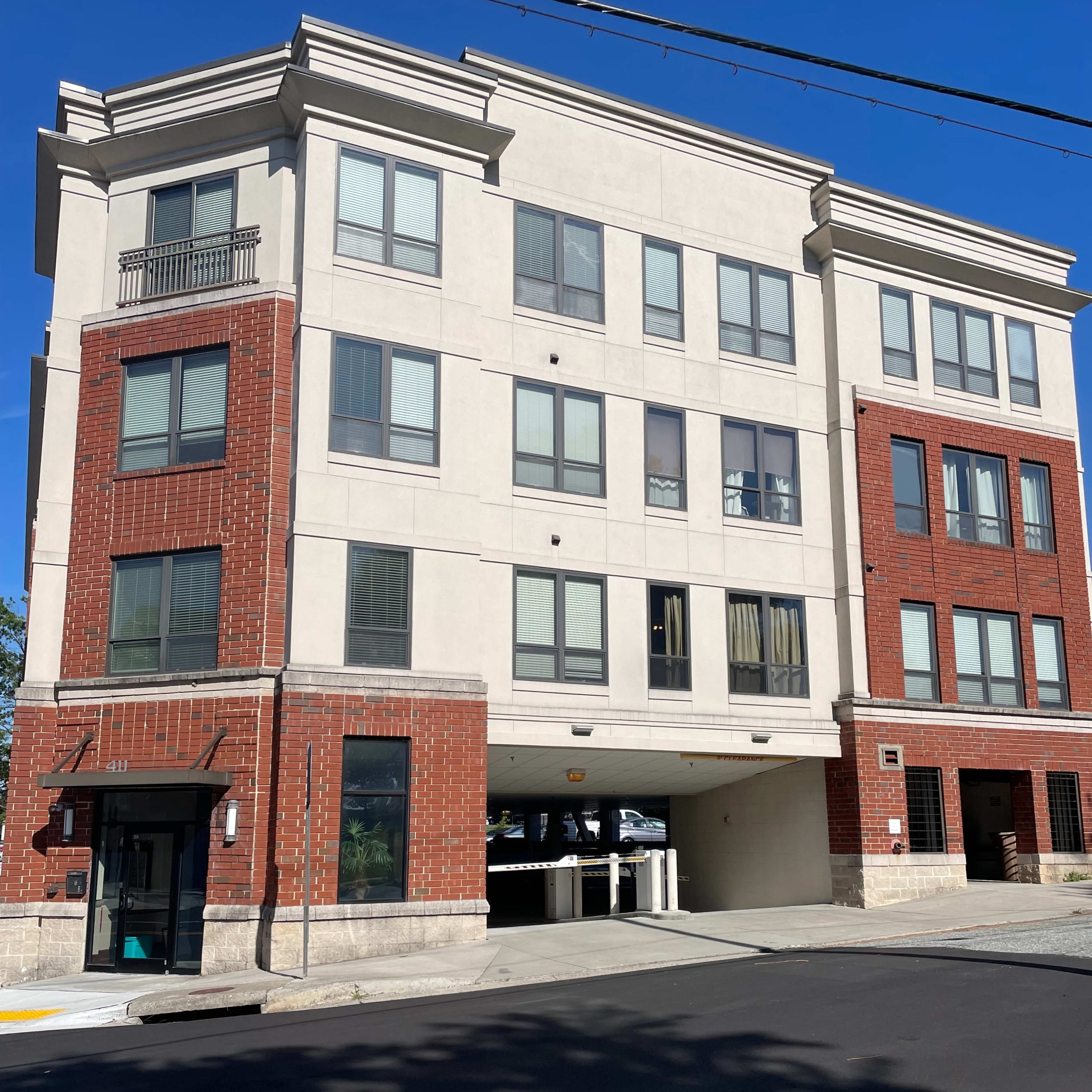 A three-story residential building features a mix of brick and stucco exteriors with parking access underneath.