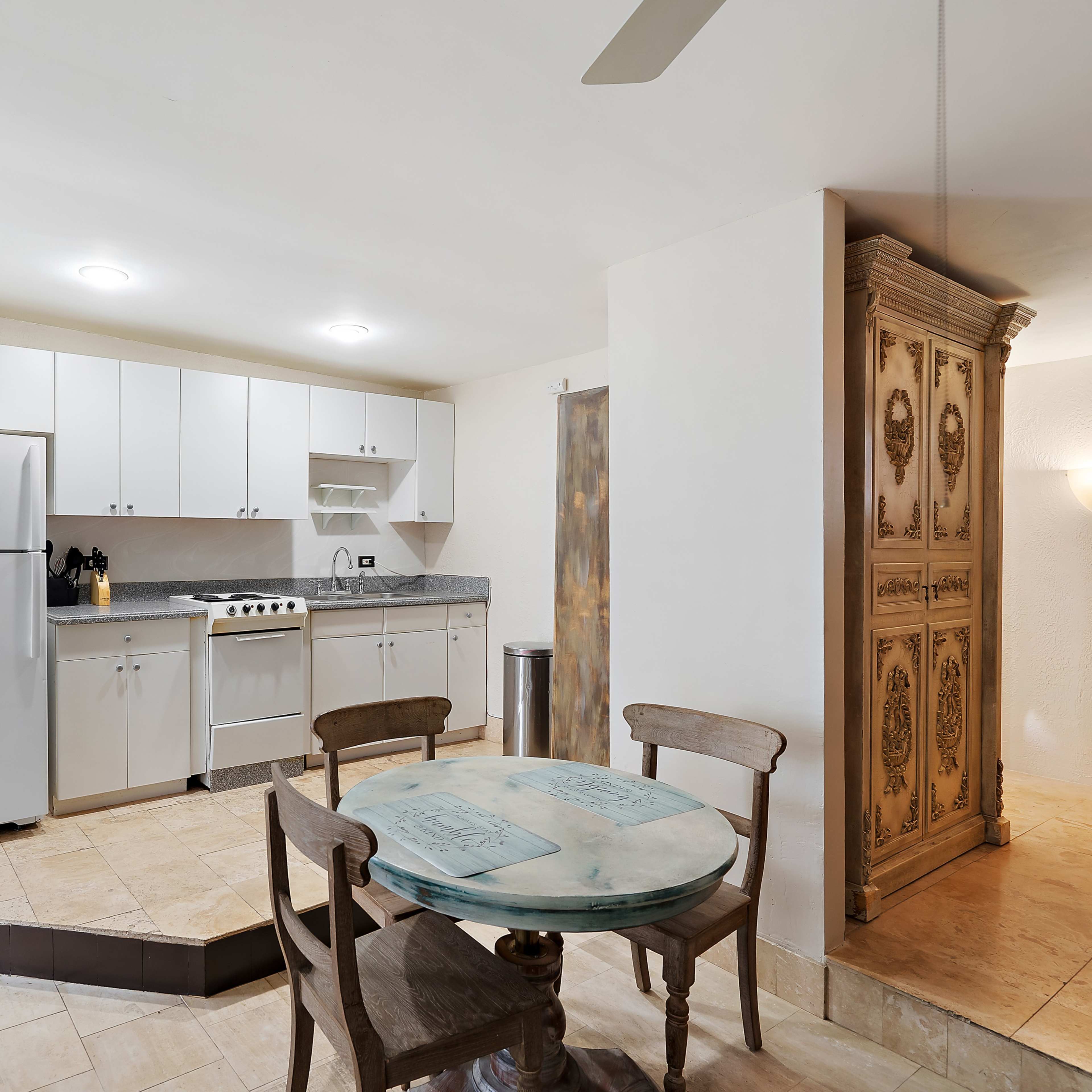 A small, modern kitchen features white cabinets, a gas stove, and a round table with wooden chairs.