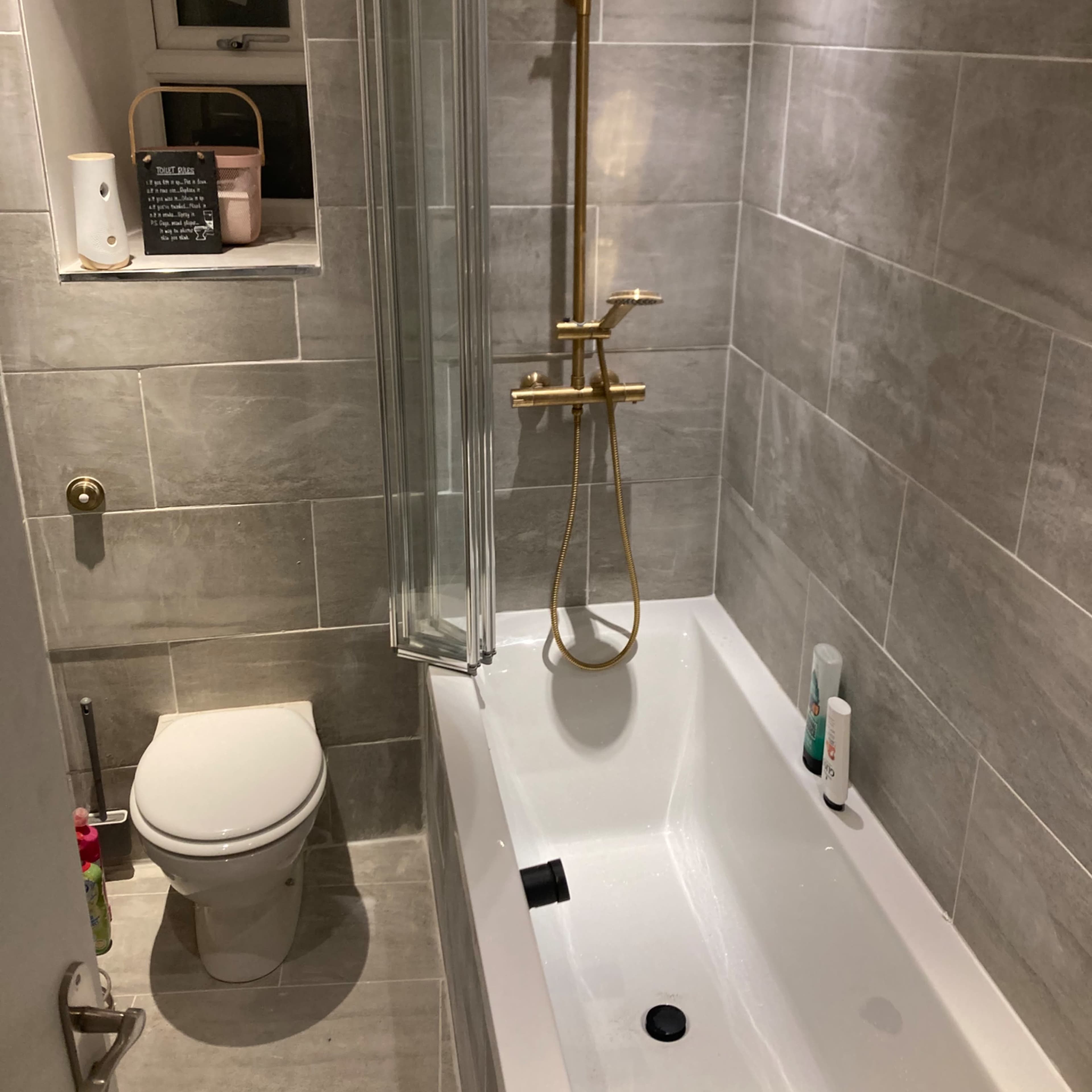 A small bathroom with a bathtub, a showerhead, and a toilet, all set against gray tiled walls.