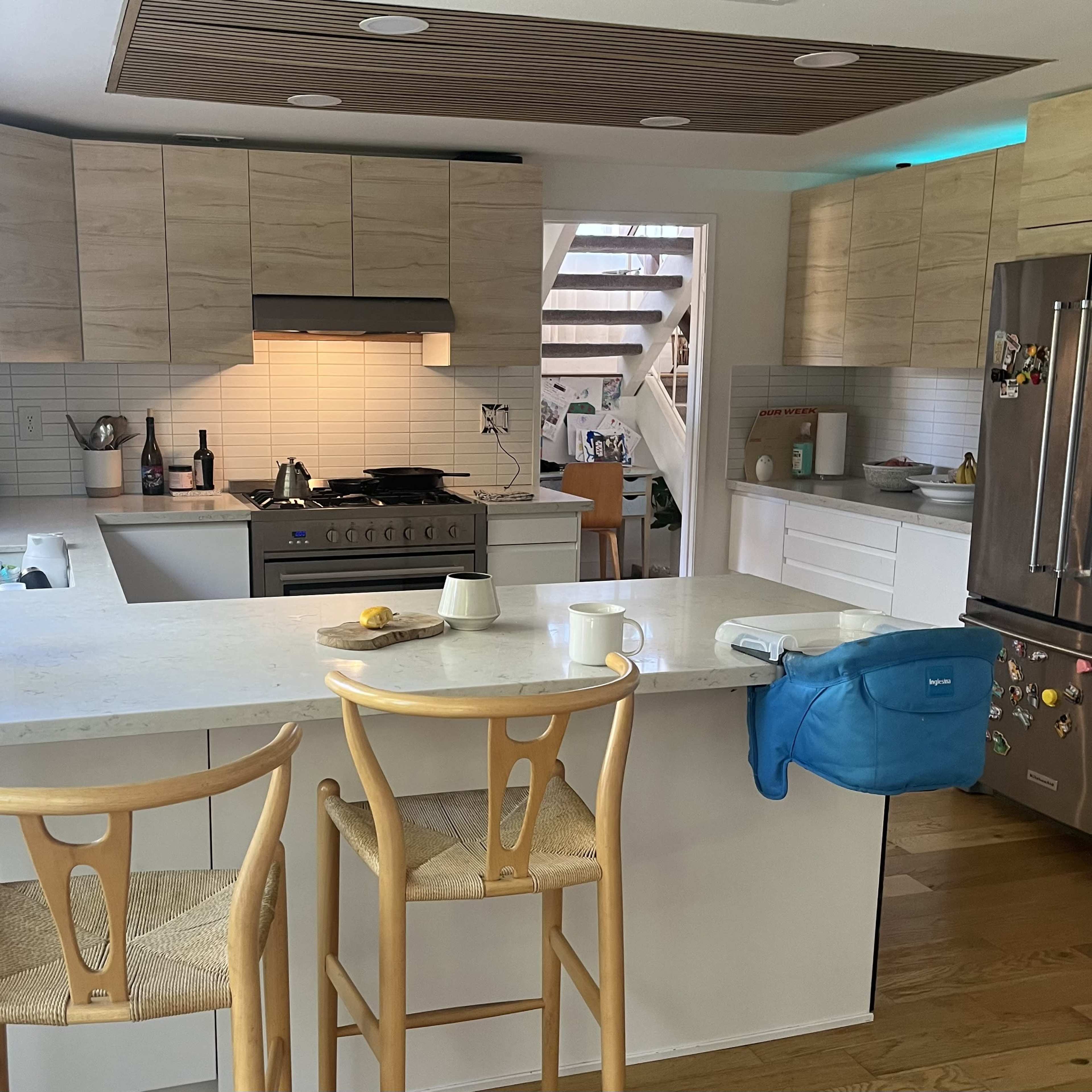 A modern kitchen with light-colored cabinetry, a central island with two wooden stools, and stainless steel appliances.