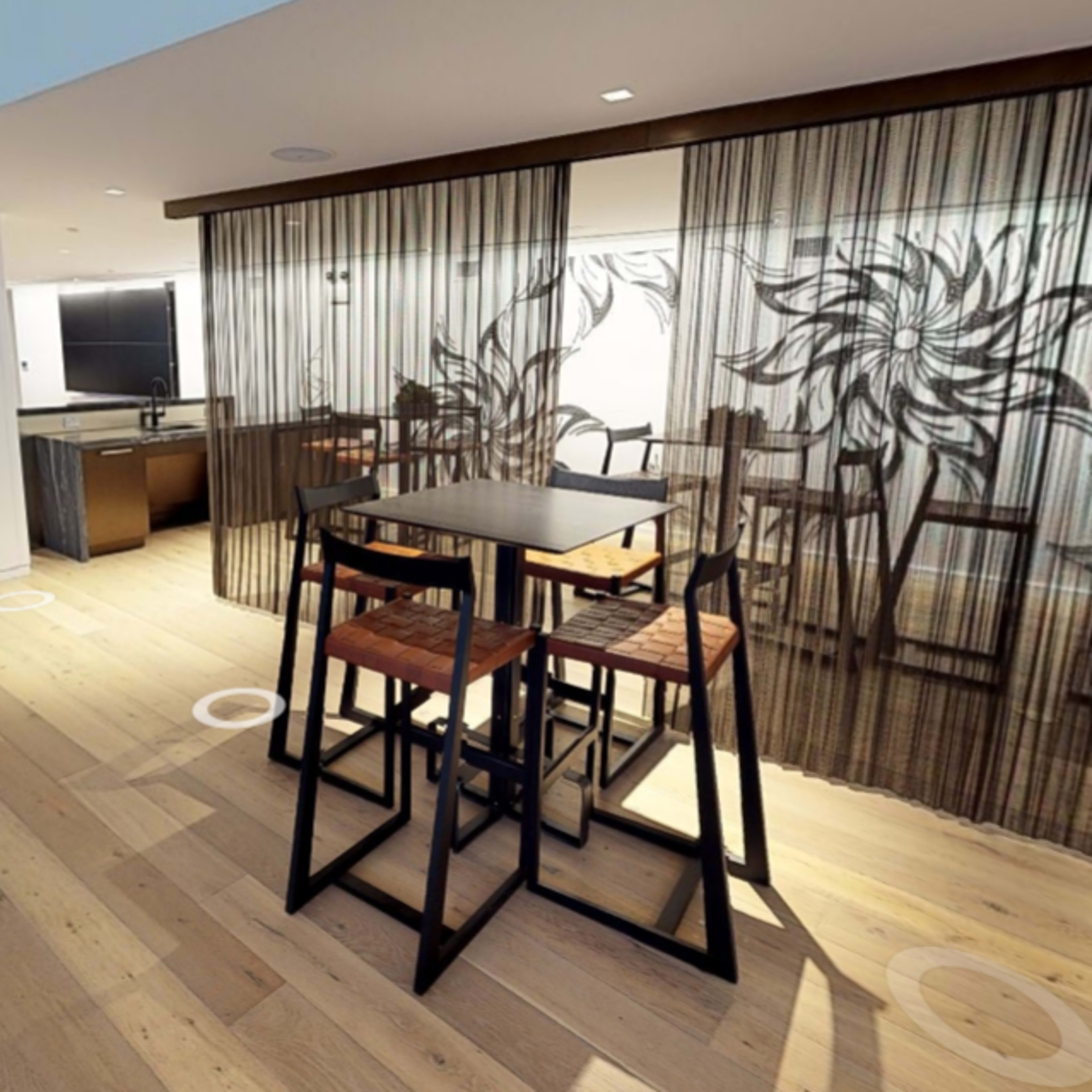 A modern interior space featuring a wooden floor, a high table with stools, and a translucent curtain with floral designs separating different areas.