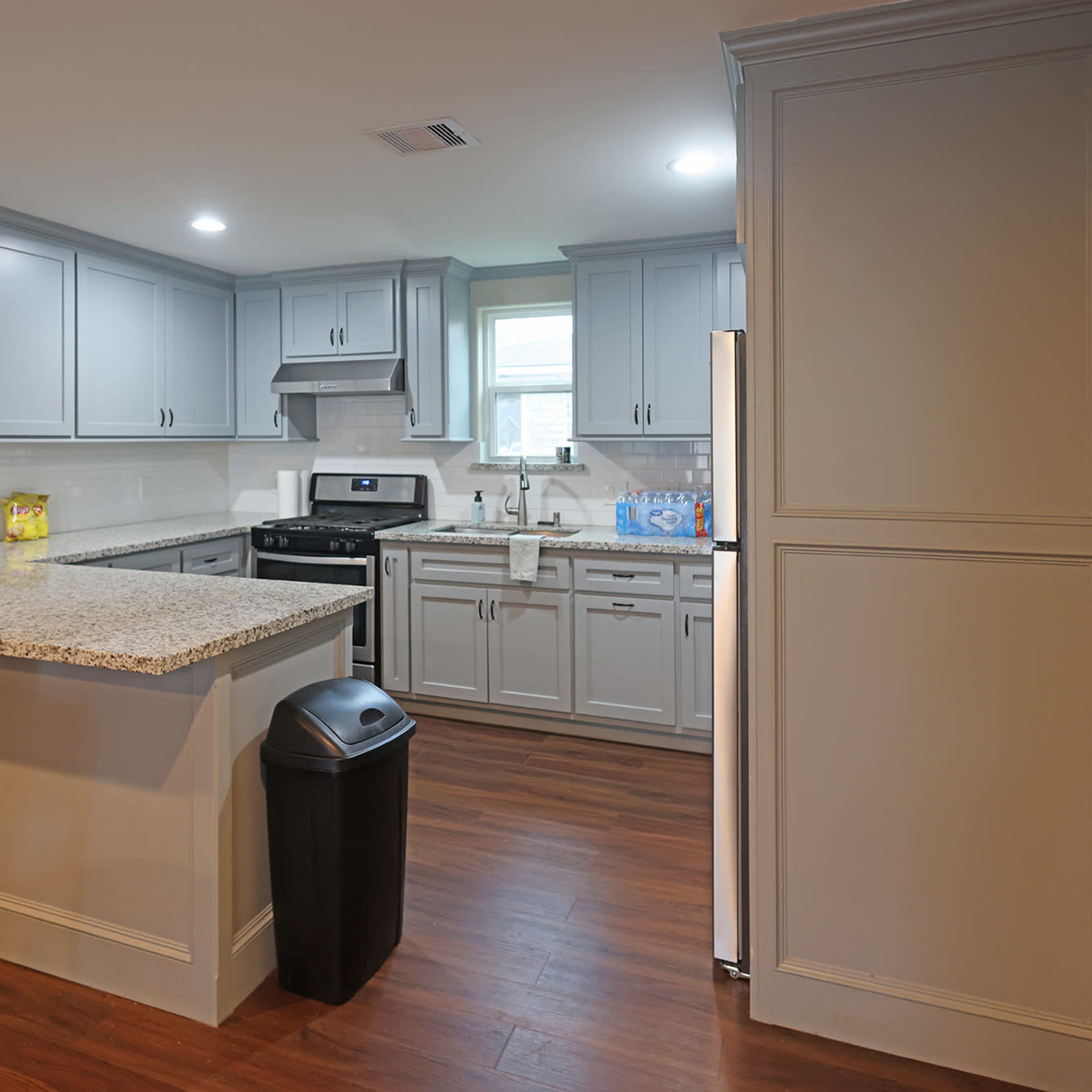 A modern kitchen with gray cabinets, a black stove, and a countertop with a granite surface, featuring wood-like flooring.