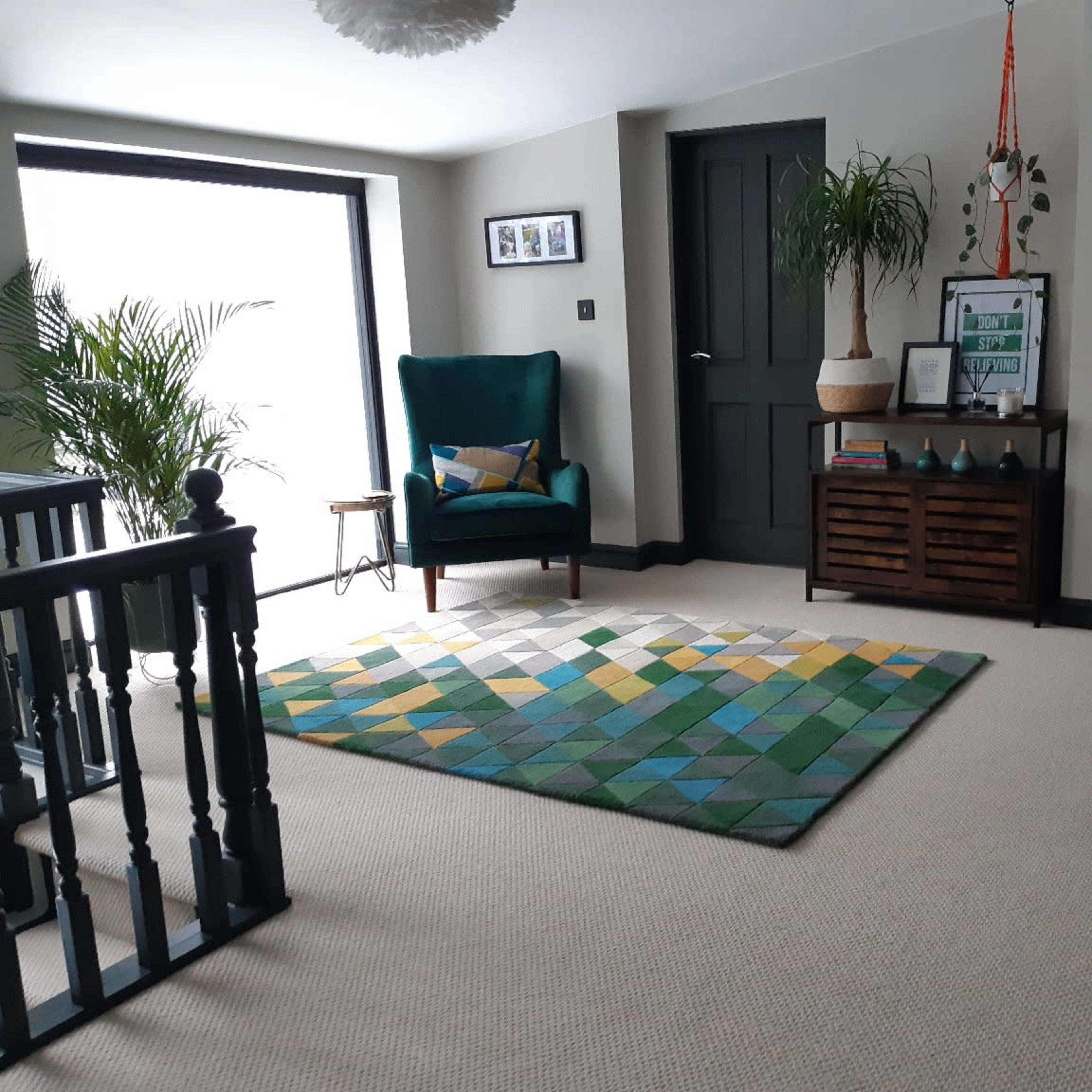 A well-lit room featuring a green armchair, a geometric patterned rug, a console table, and two doors against a neutral wall.