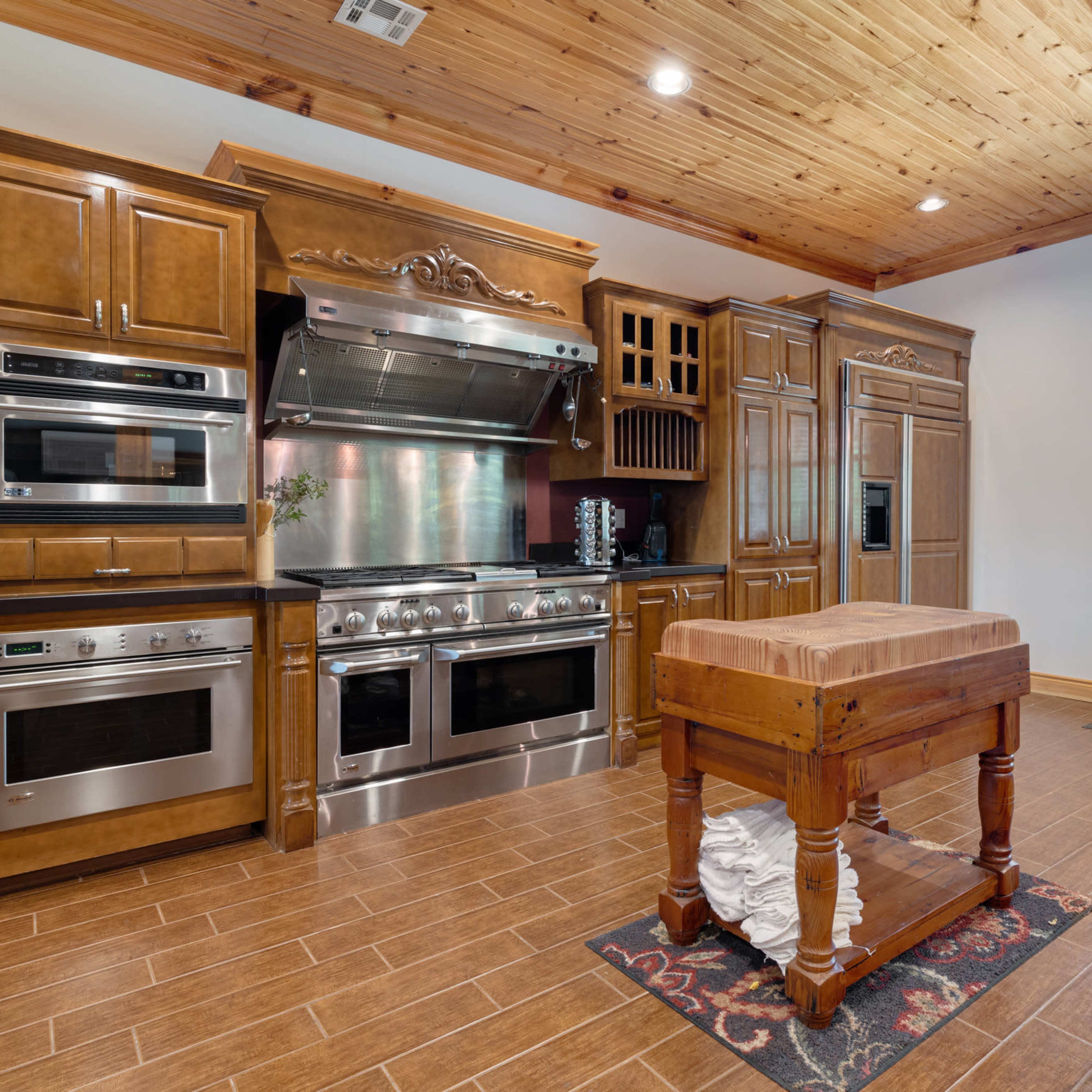 A kitchen with wooden cabinetry, stainless steel appliances, and a central wooden island.