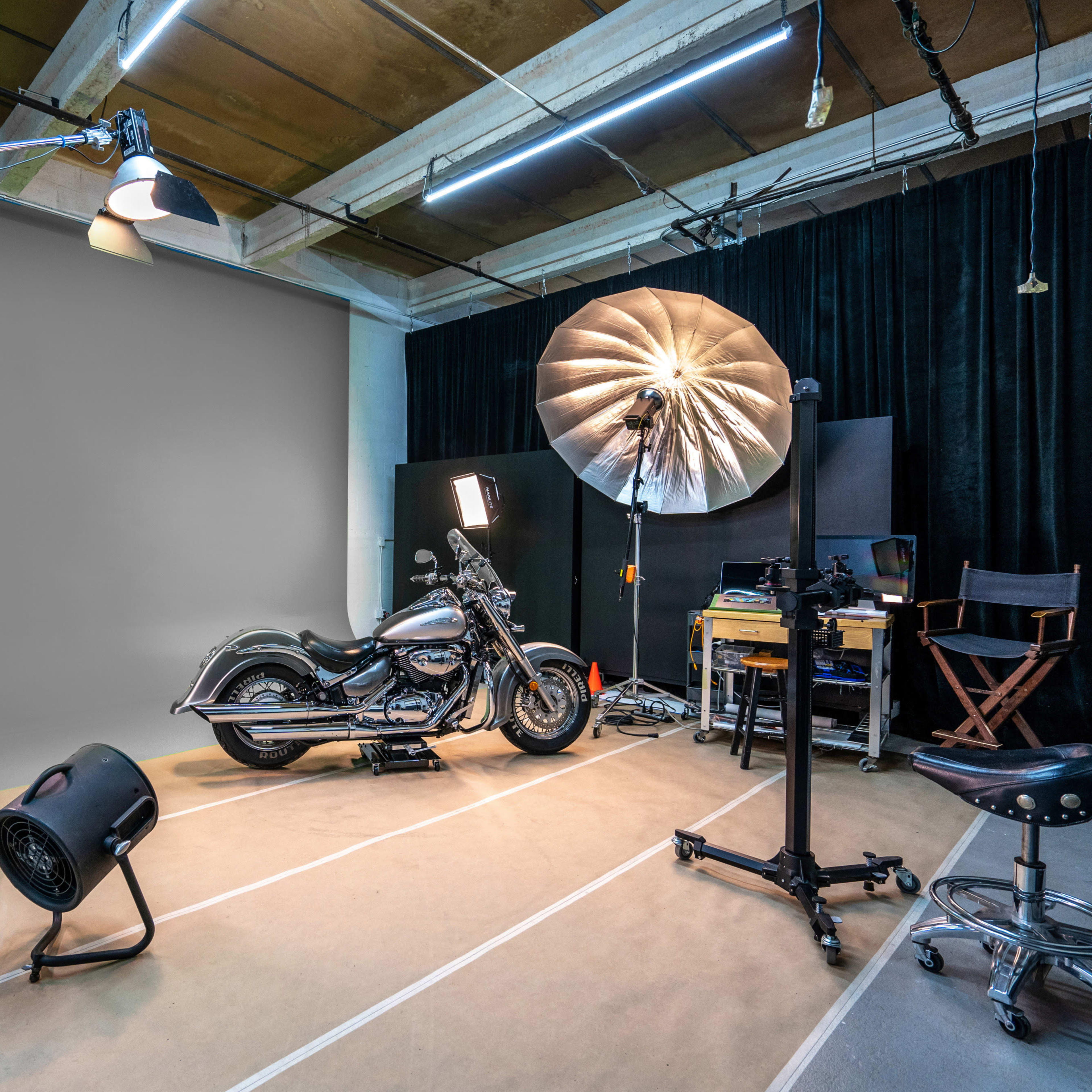 A motorcycle is positioned in a studio setup with various lighting equipment and a grey backdrop.