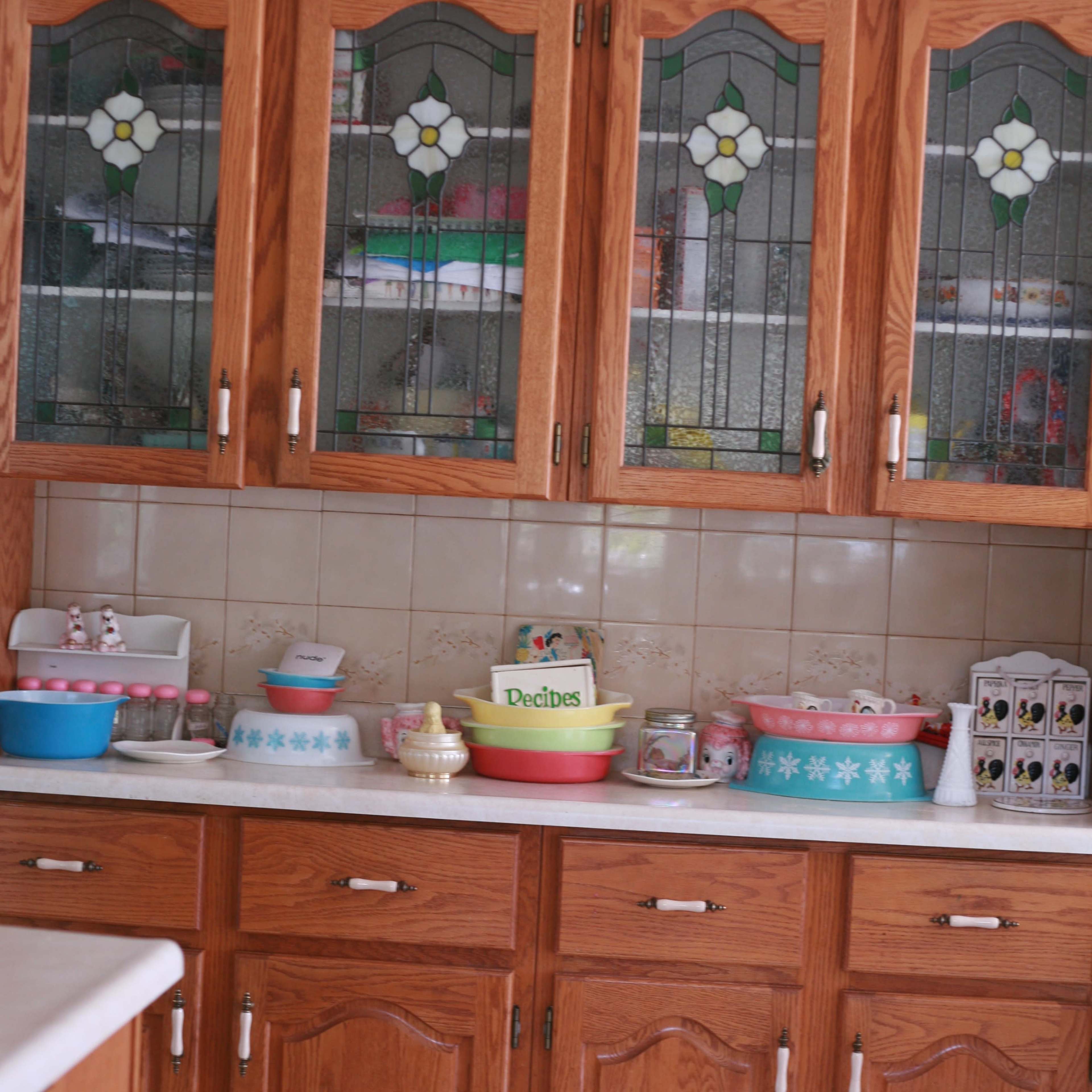 A kitchen with wooden cabinets featuring glass panels, displaying various colorful bowls and containers on a countertop.