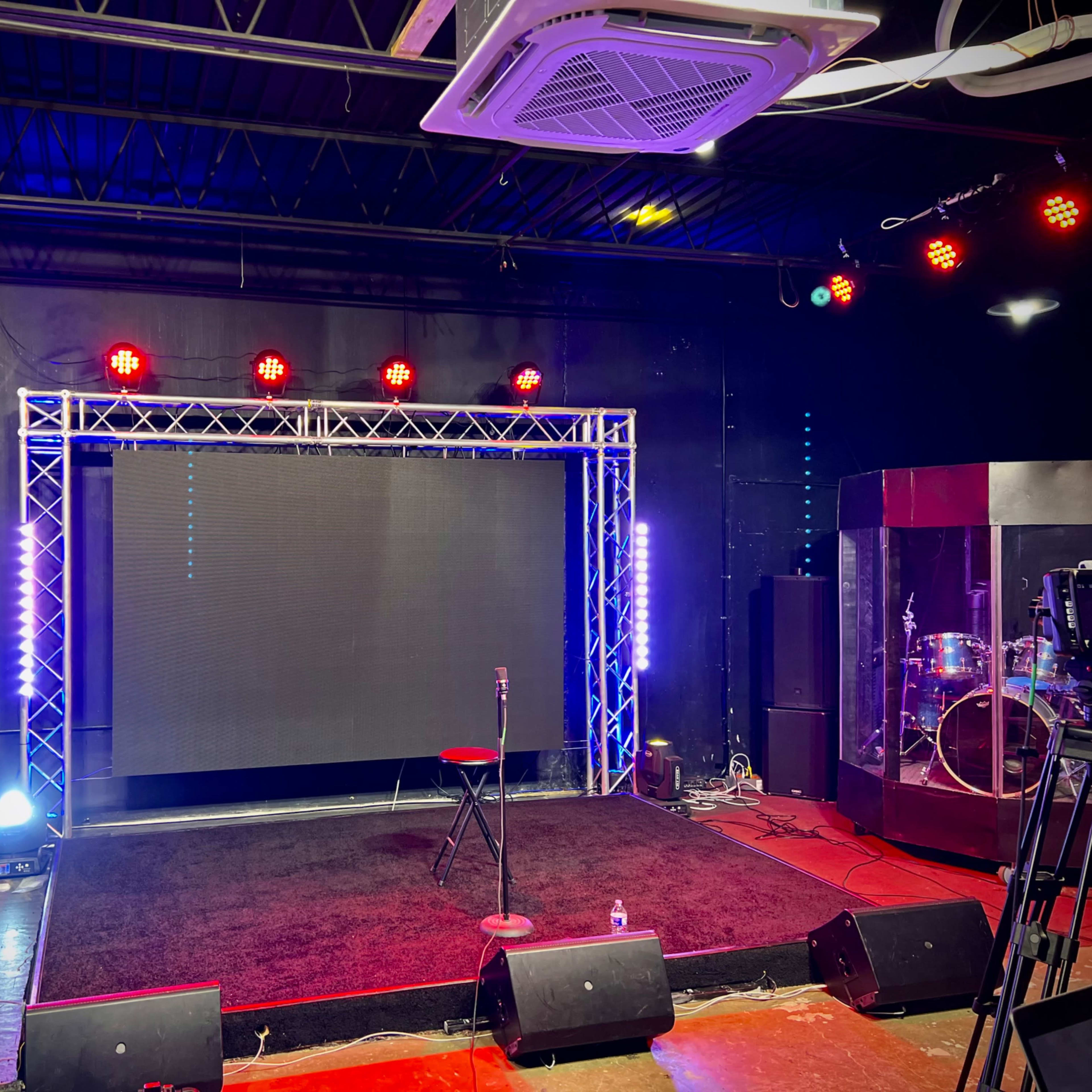 A performance stage with a black background, a red stool, spotlights, and sound equipment set up for a show.