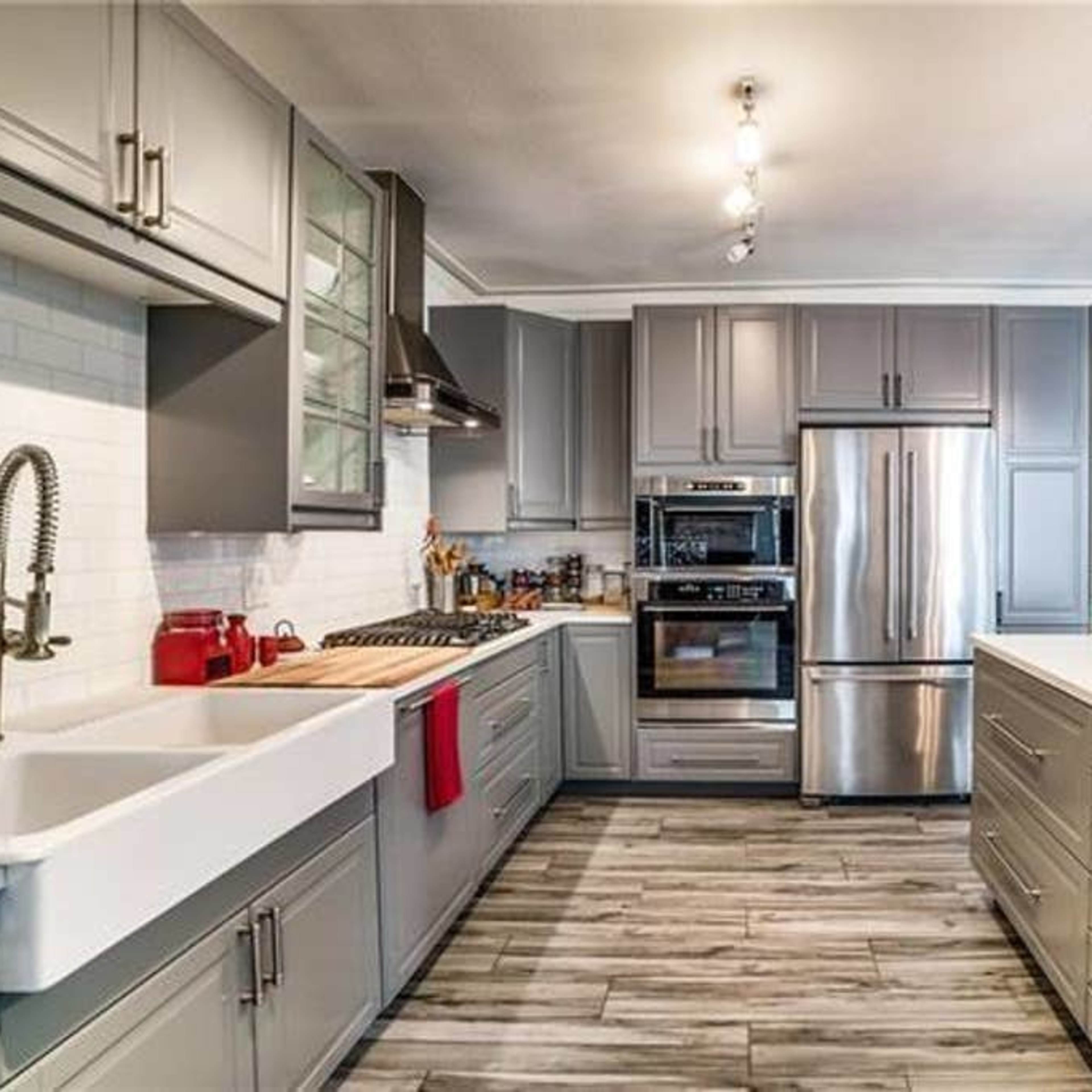 A modern kitchen featuring gray cabinets, stainless steel appliances, and a large central island with a white countertop.