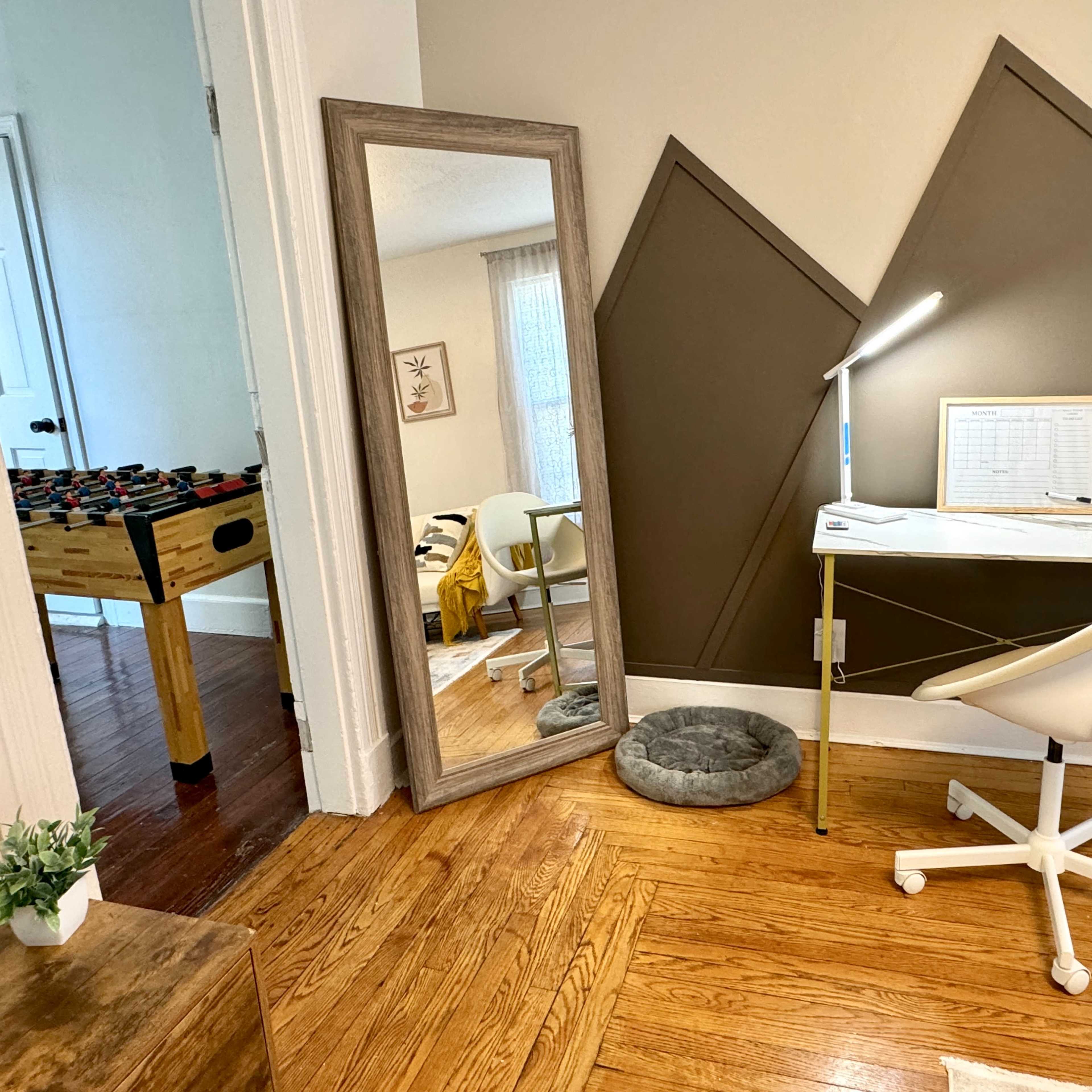 A small interior space featuring a desk with a chair, a large mirror, and a foosball table in the background.
