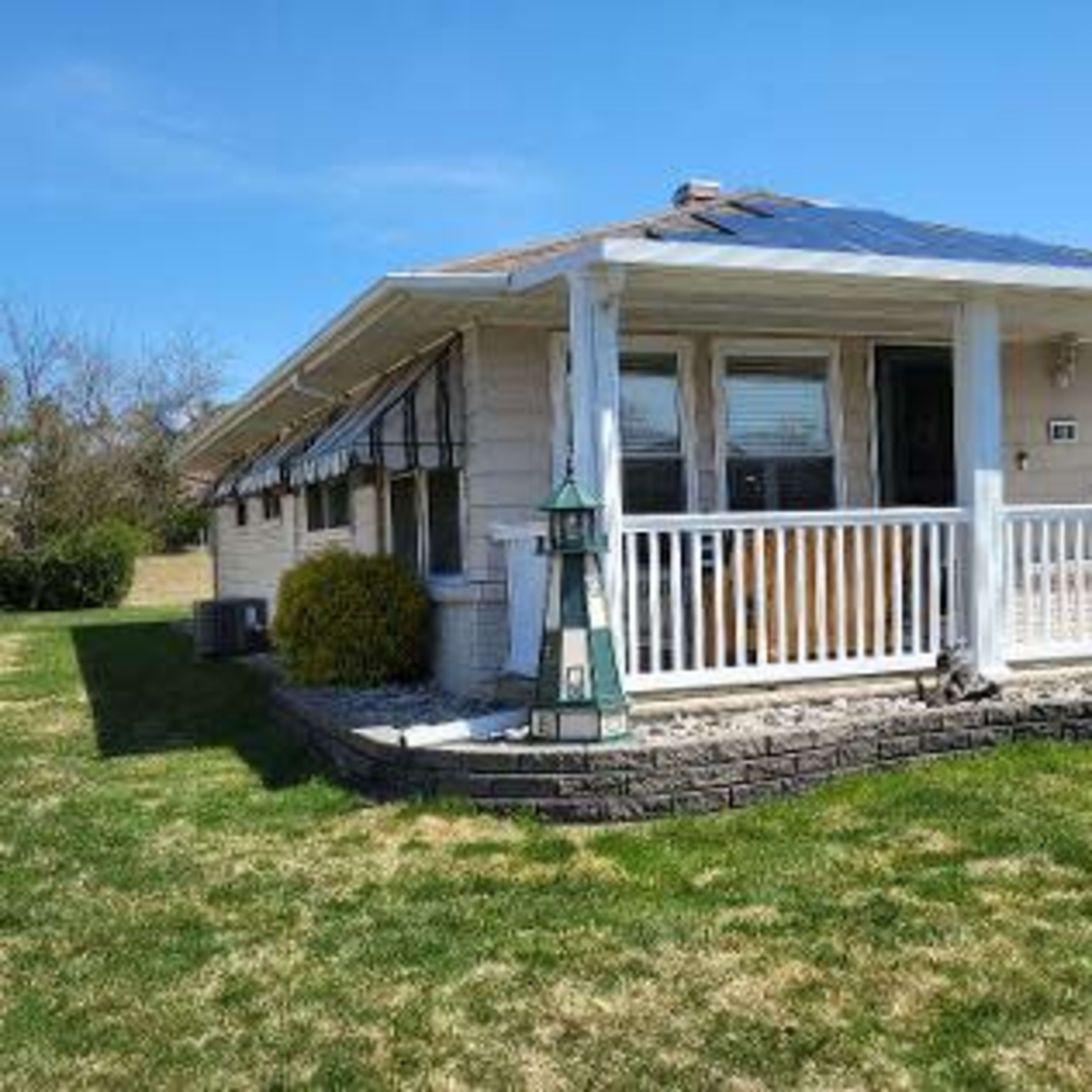 A single-story house with a porch is surrounded by green grass and bushes.