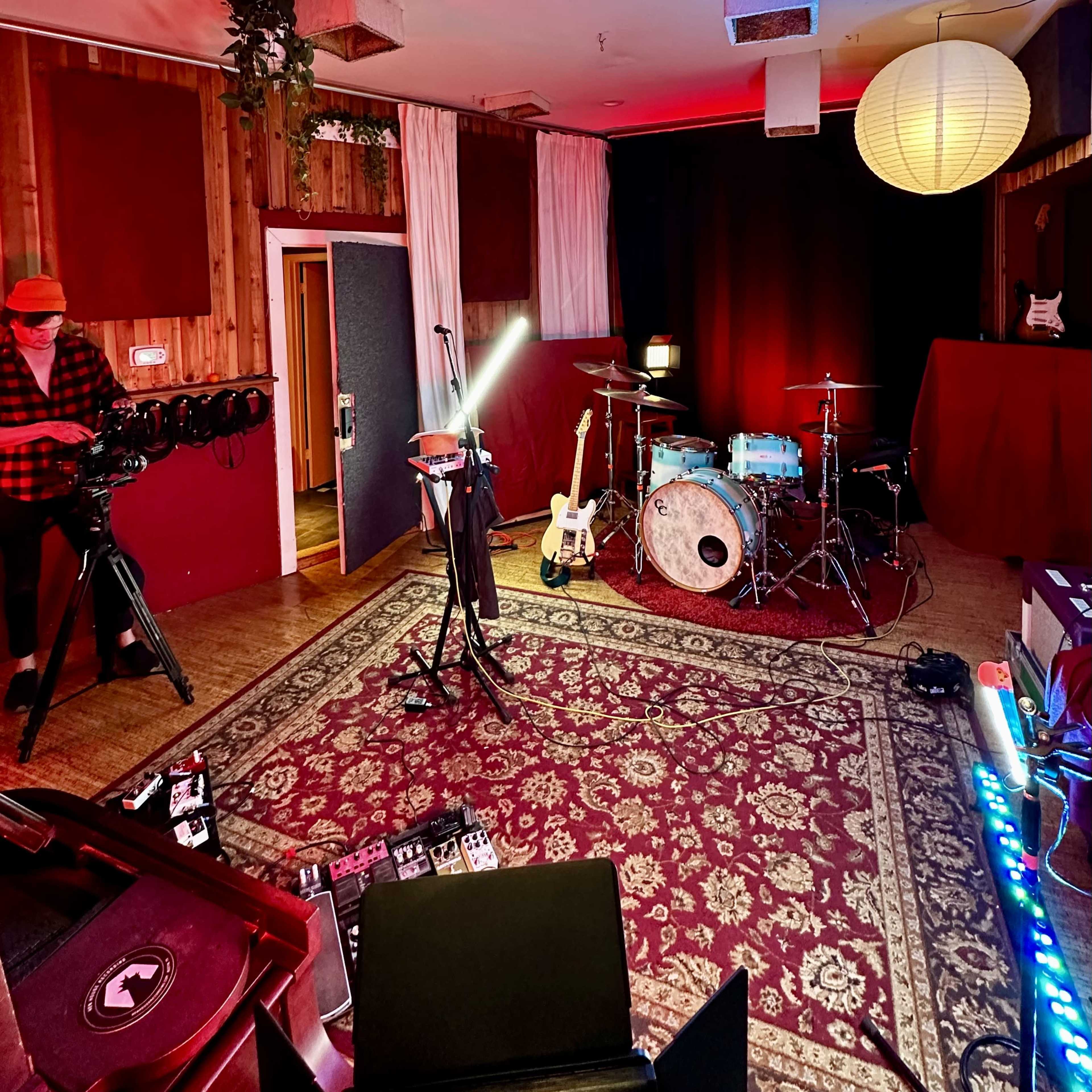 A music studio setup with instruments, including a drum kit and guitar, surrounded by various equipment and soft lighting.