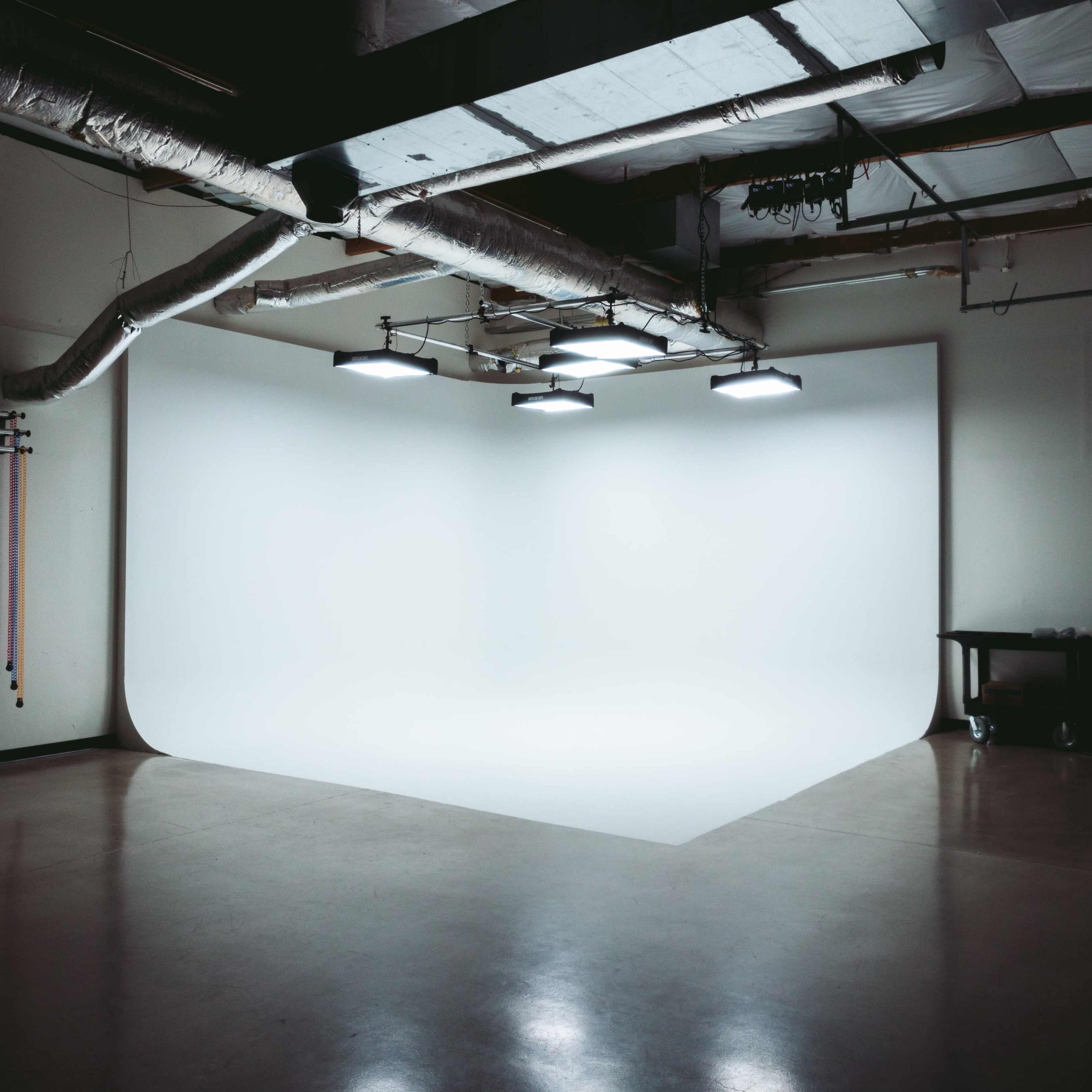 A spacious studio features a seamless white backdrop illuminated by overhead lights.