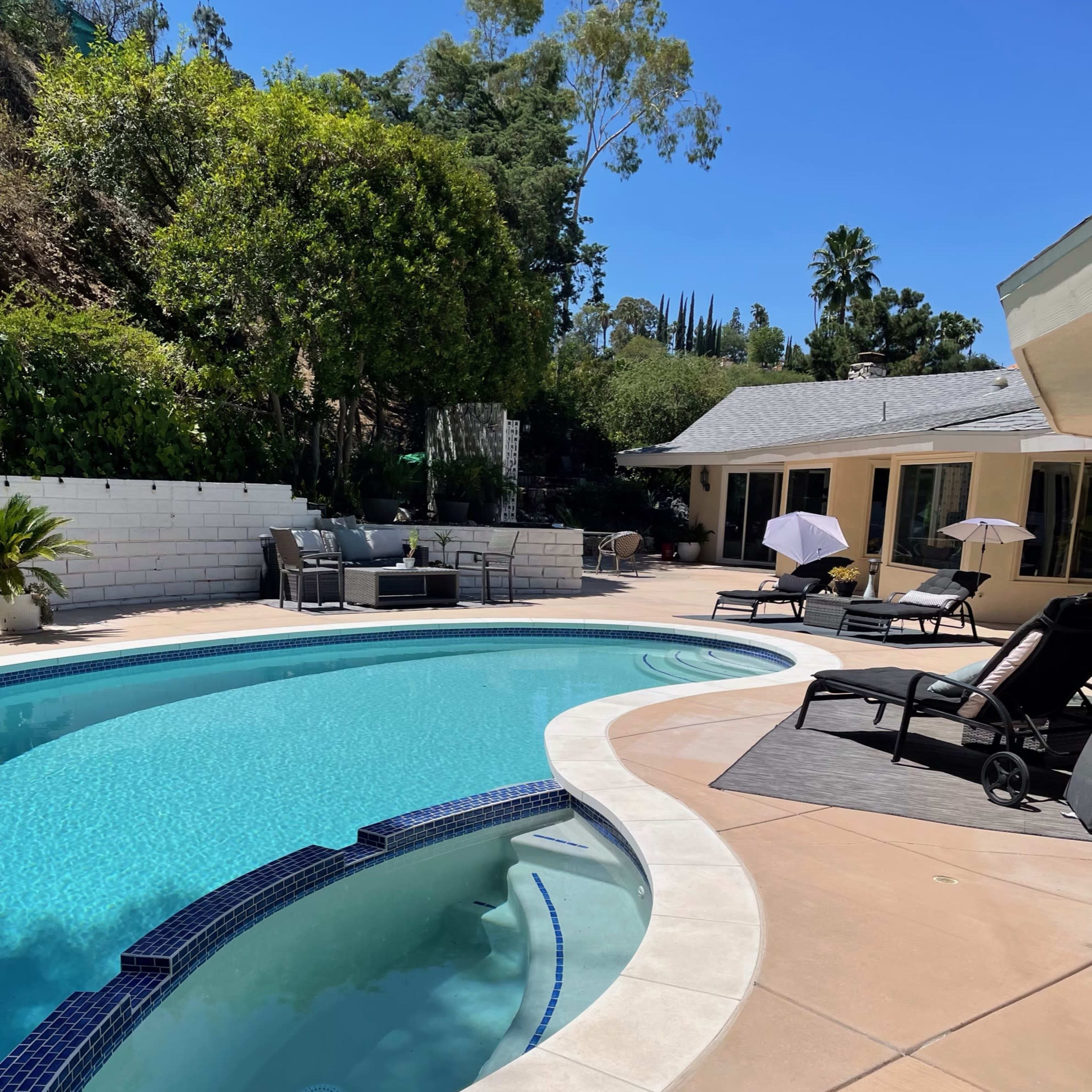 A well-maintained pool area surrounded by lounge chairs and umbrellas in a sunny backyard.