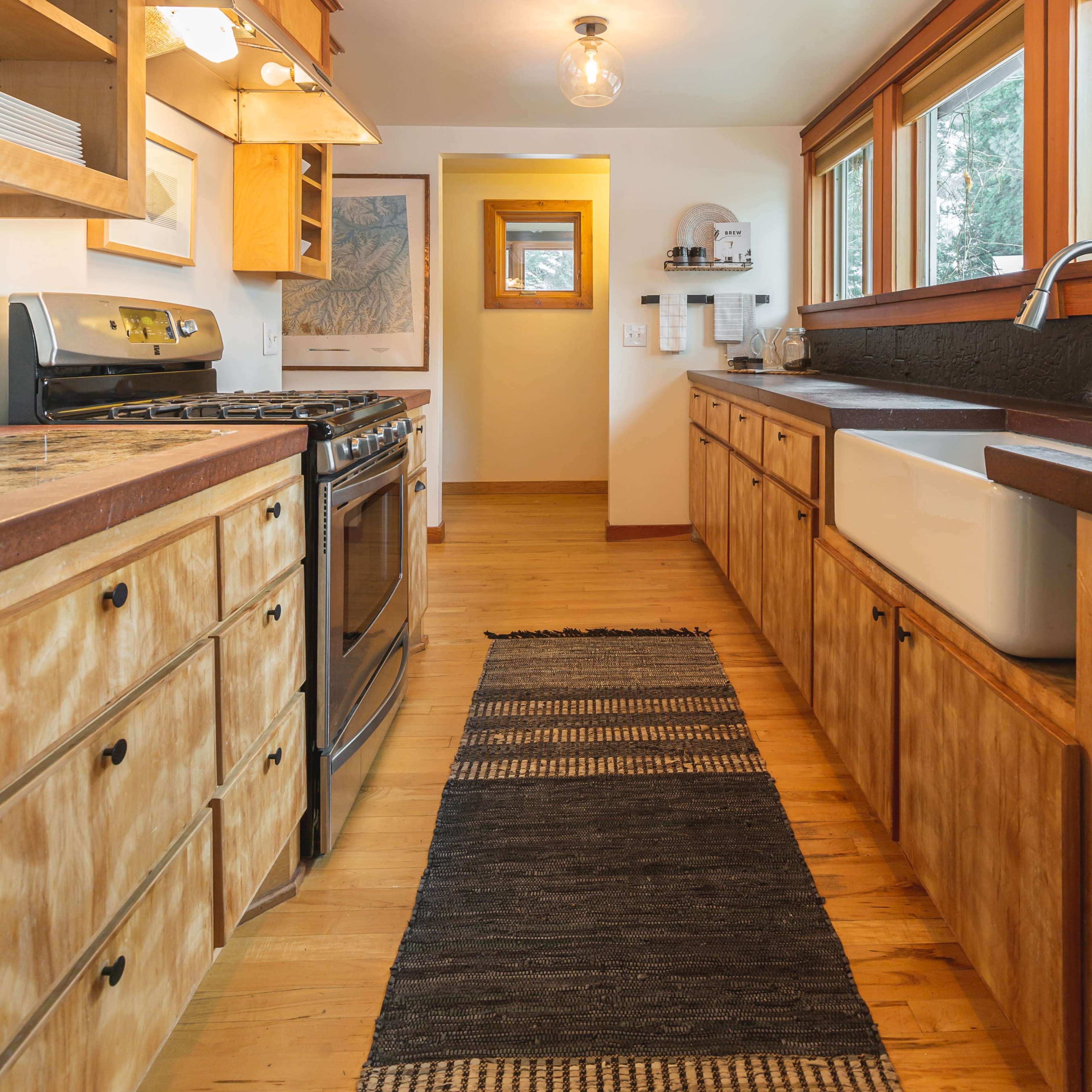 A kitchen with wooden cabinets, a large farmhouse sink, and a long black runner rug along the floor.