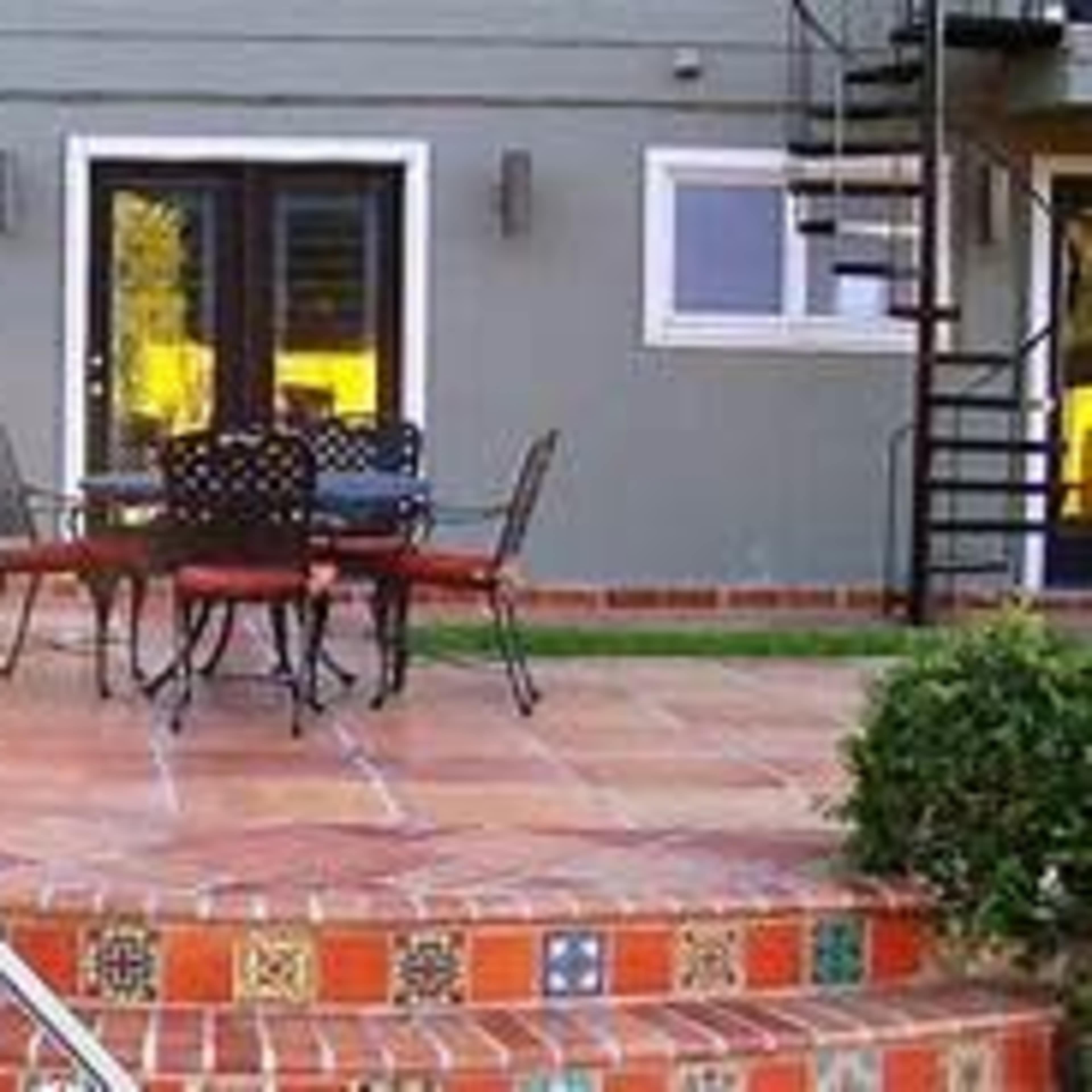 A patio area features a round table with four chairs, surrounded by decorative tiled steps leading to a gray building.