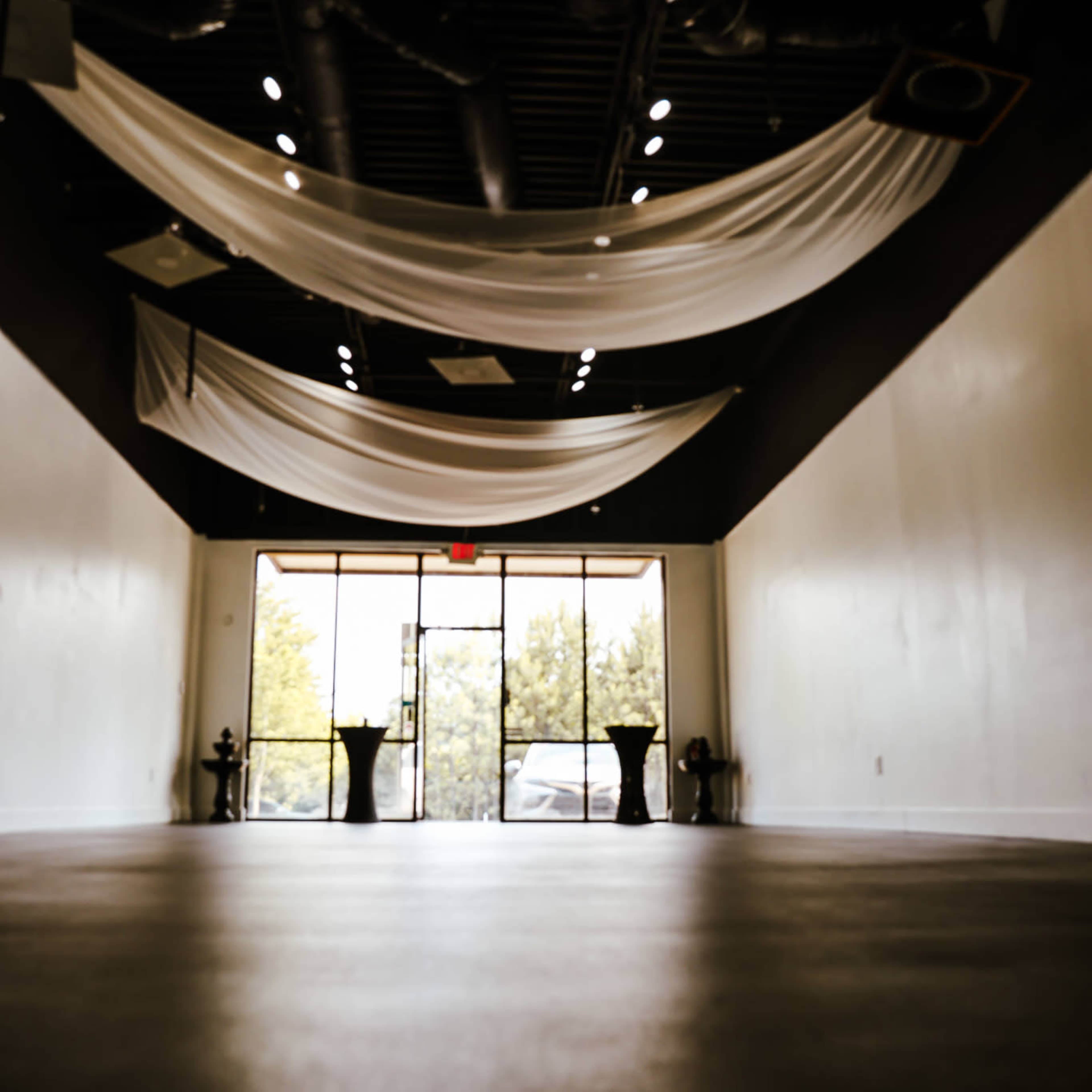 An empty indoor space with draped white fabric on the ceiling and large glass doors leading to the outside.