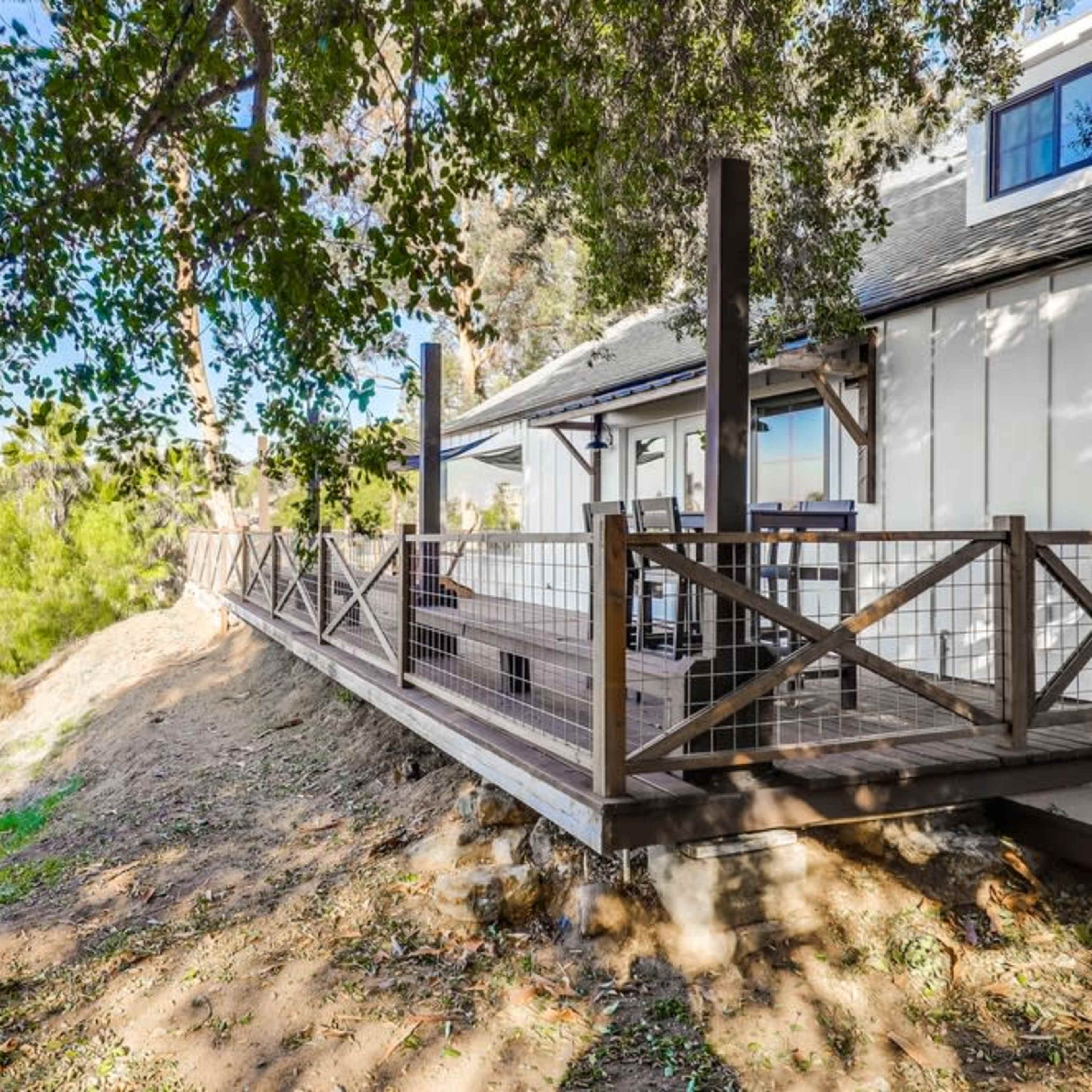 A wooden deck extends from a house, overlooking a hillside covered in greenery.