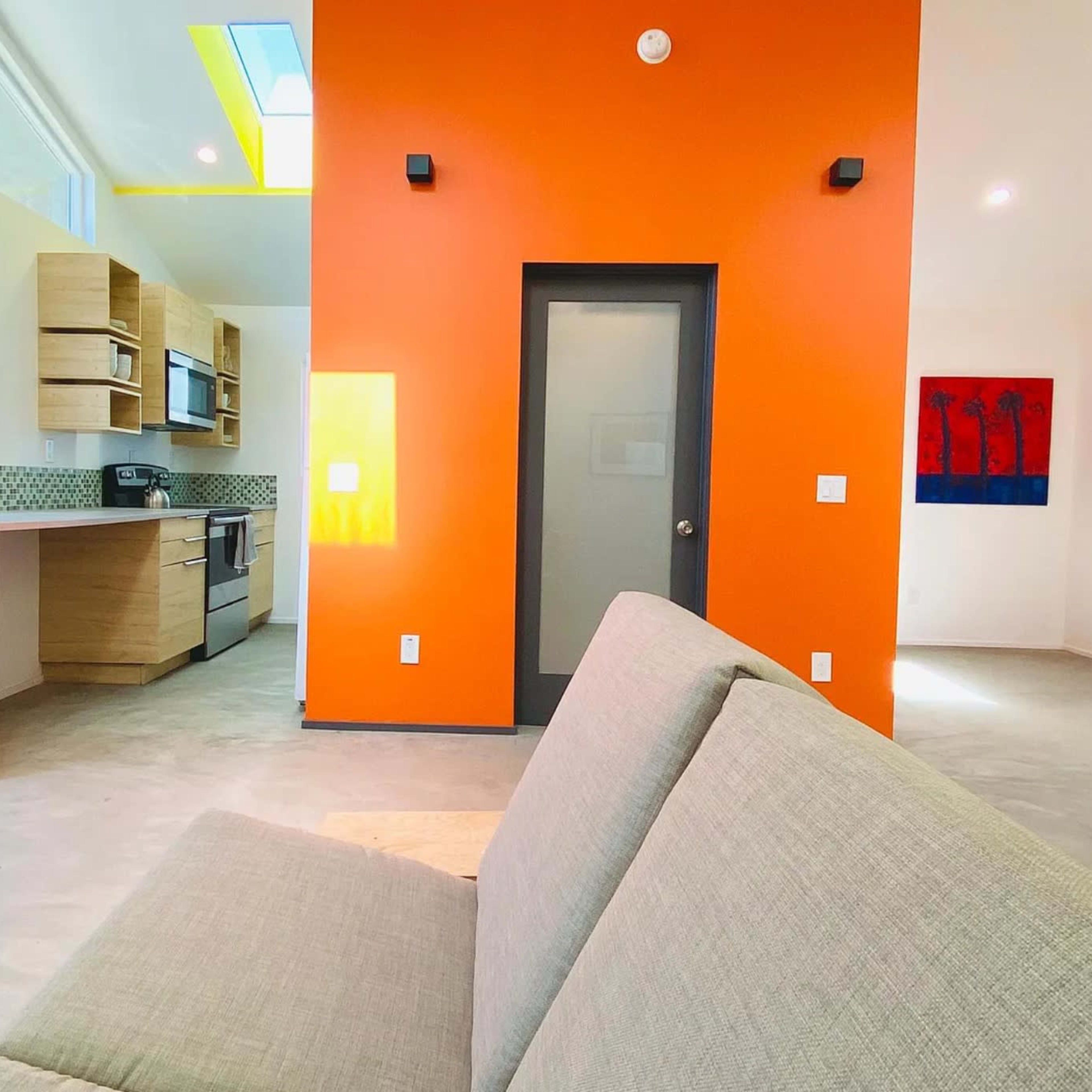 A modern, open-concept living space with a kitchen area on the left and a bright orange accent wall.