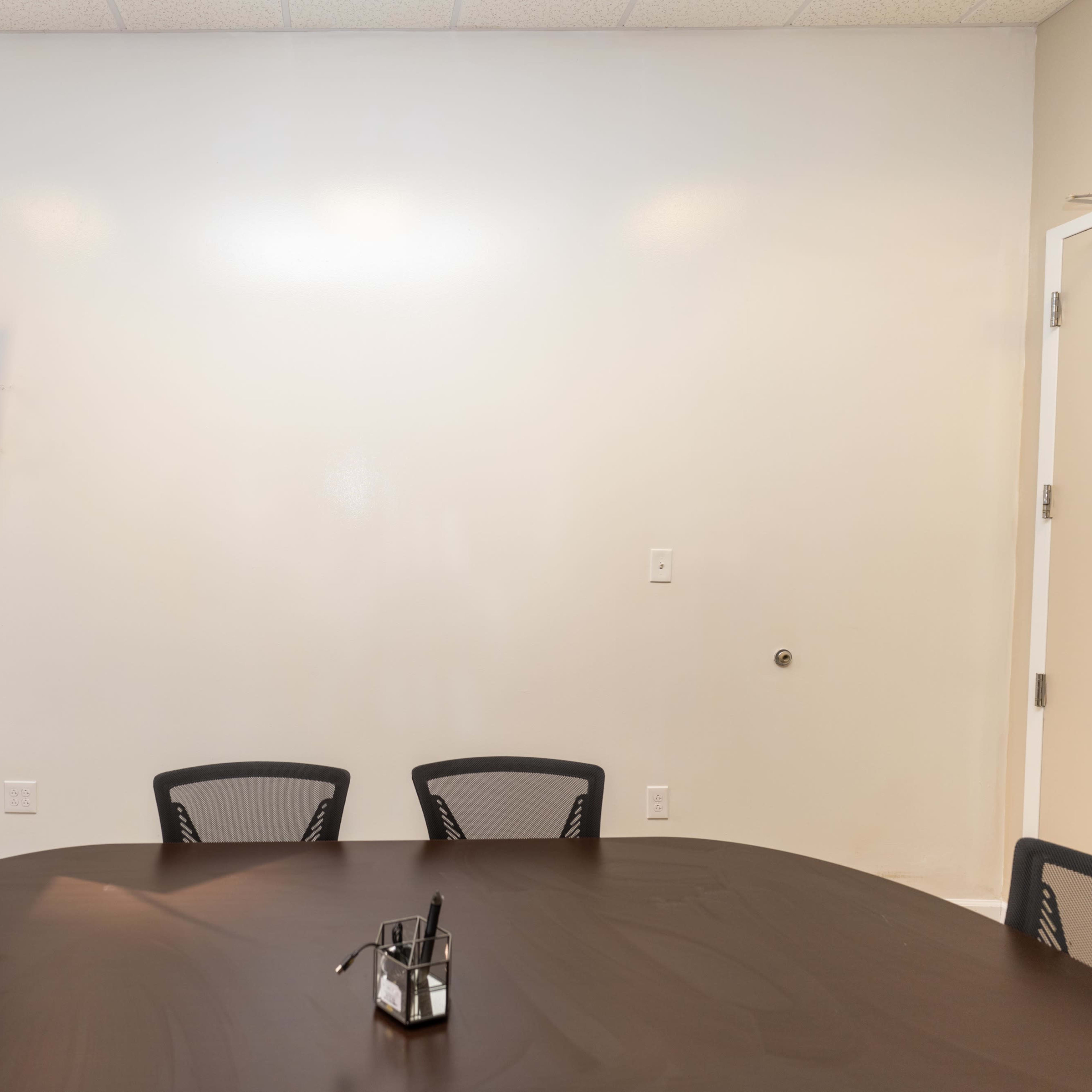 A large, round table is placed in a minimally decorated meeting room with a television mounted on the wall.